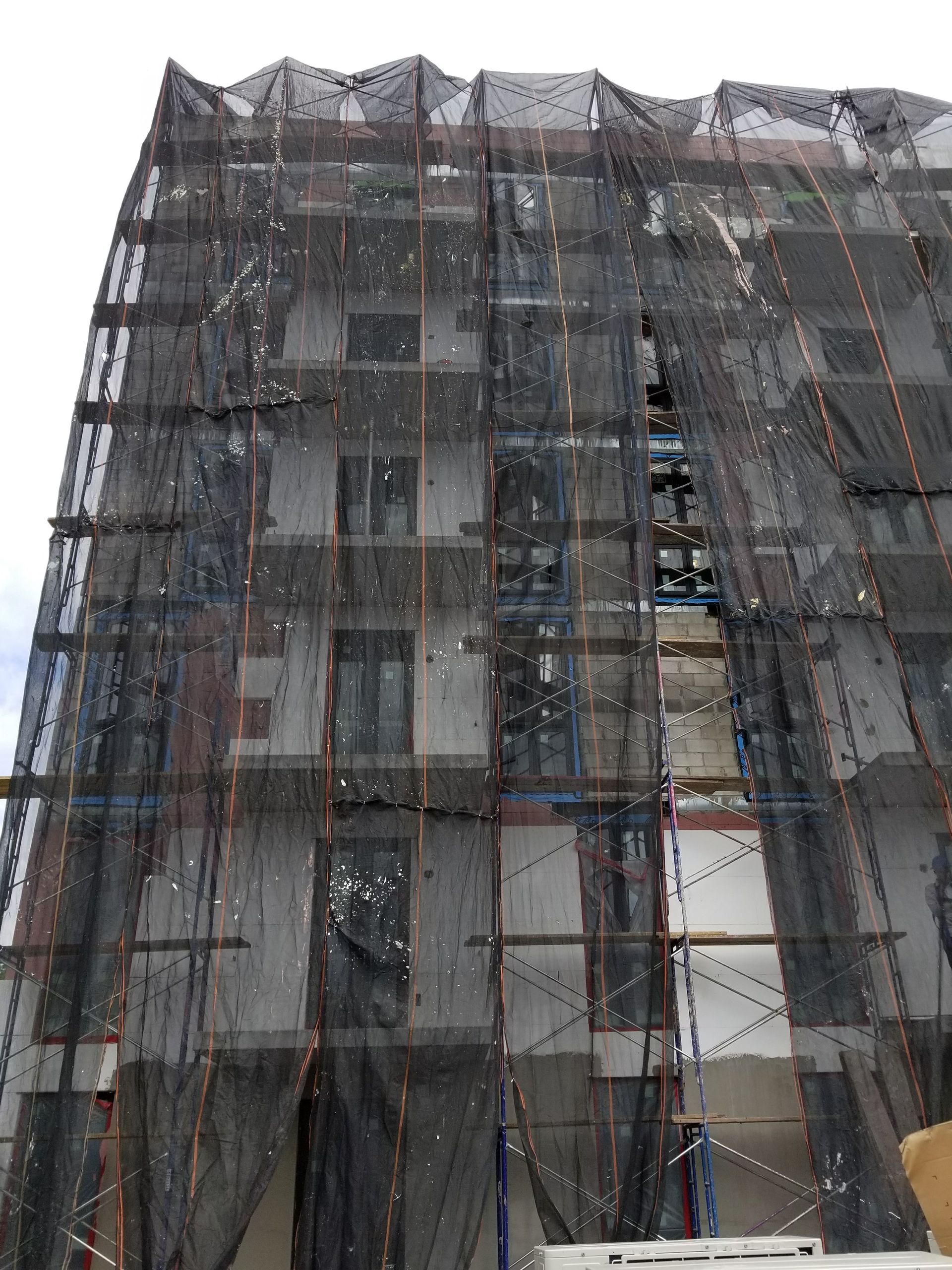 Building under construction, covered in black safety netting.