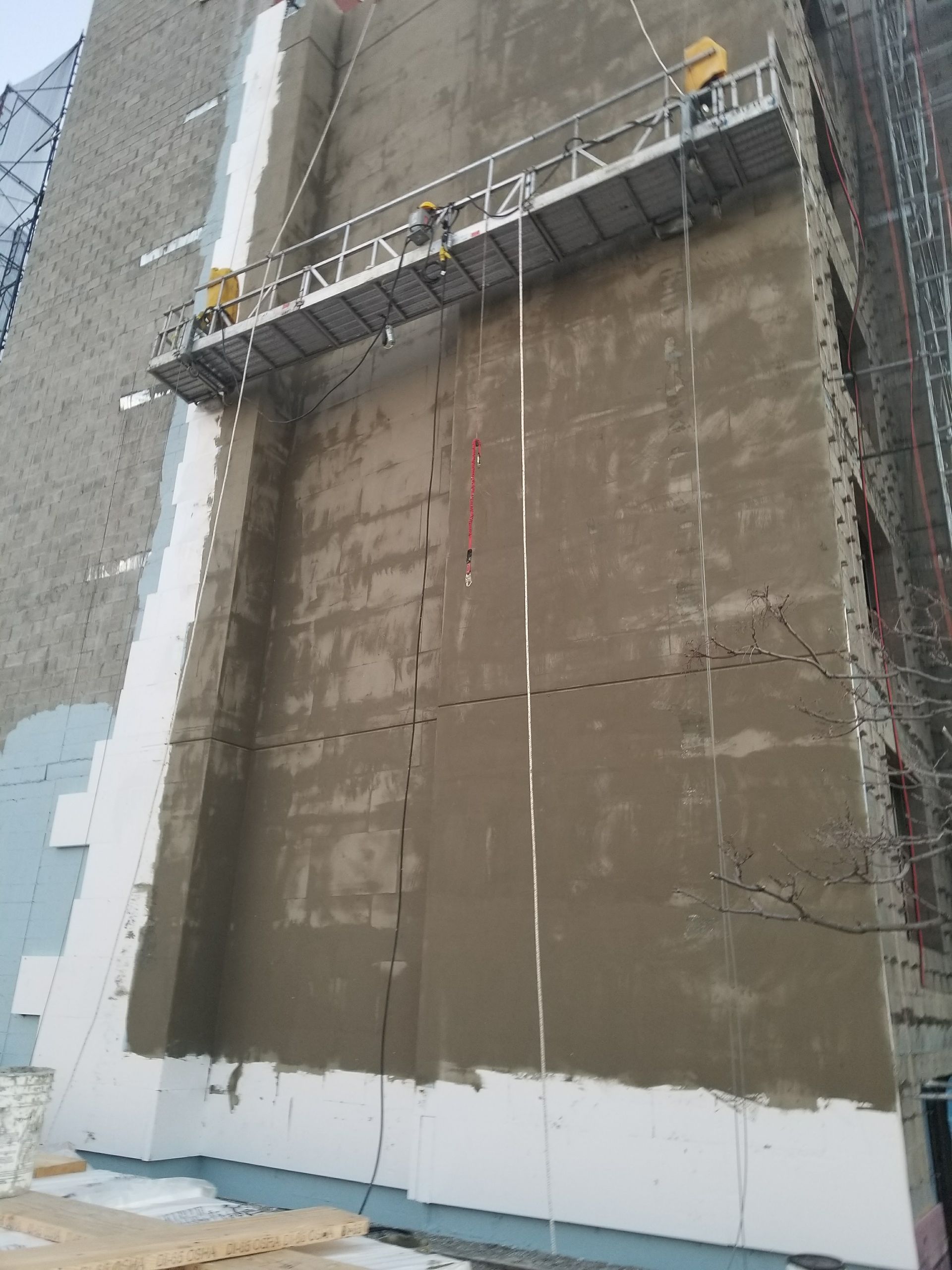 Workers on a suspended scaffold applying stucco to a building facade.
