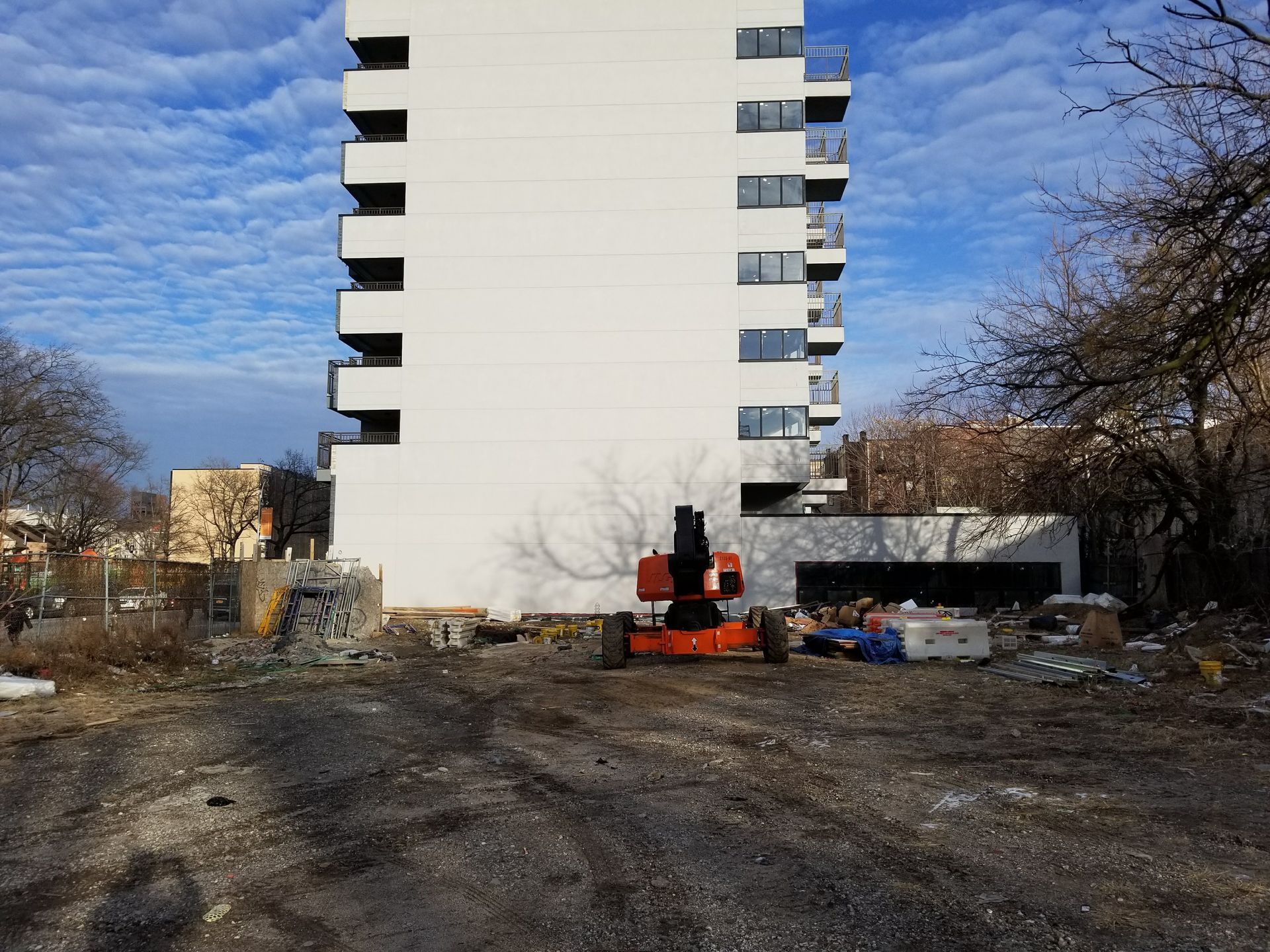 A tall white building with balconies and an orange lift on a construction site.