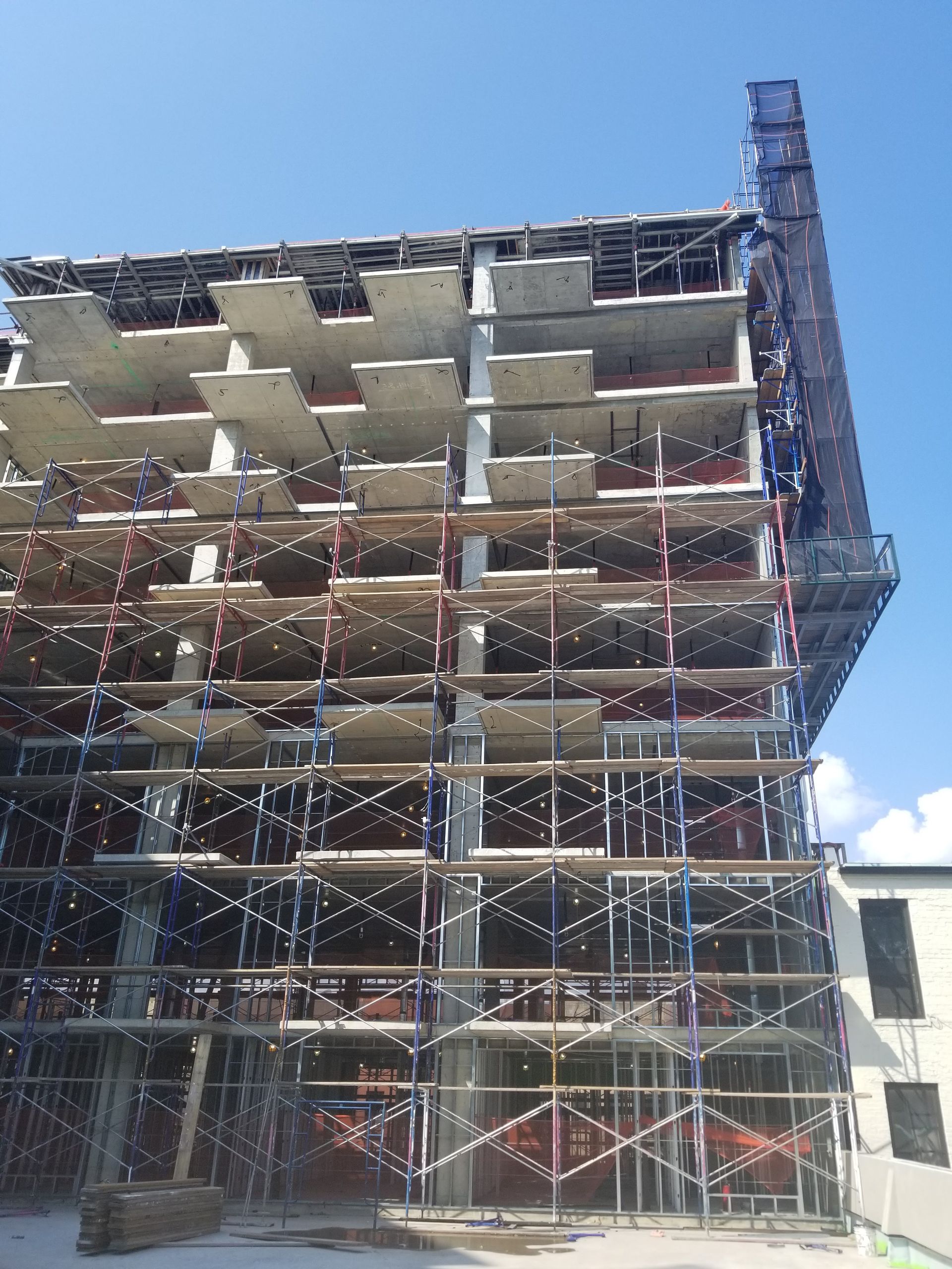 Construction site of a multi-story building. Scaffolding surrounds the structure, blue sky in background.