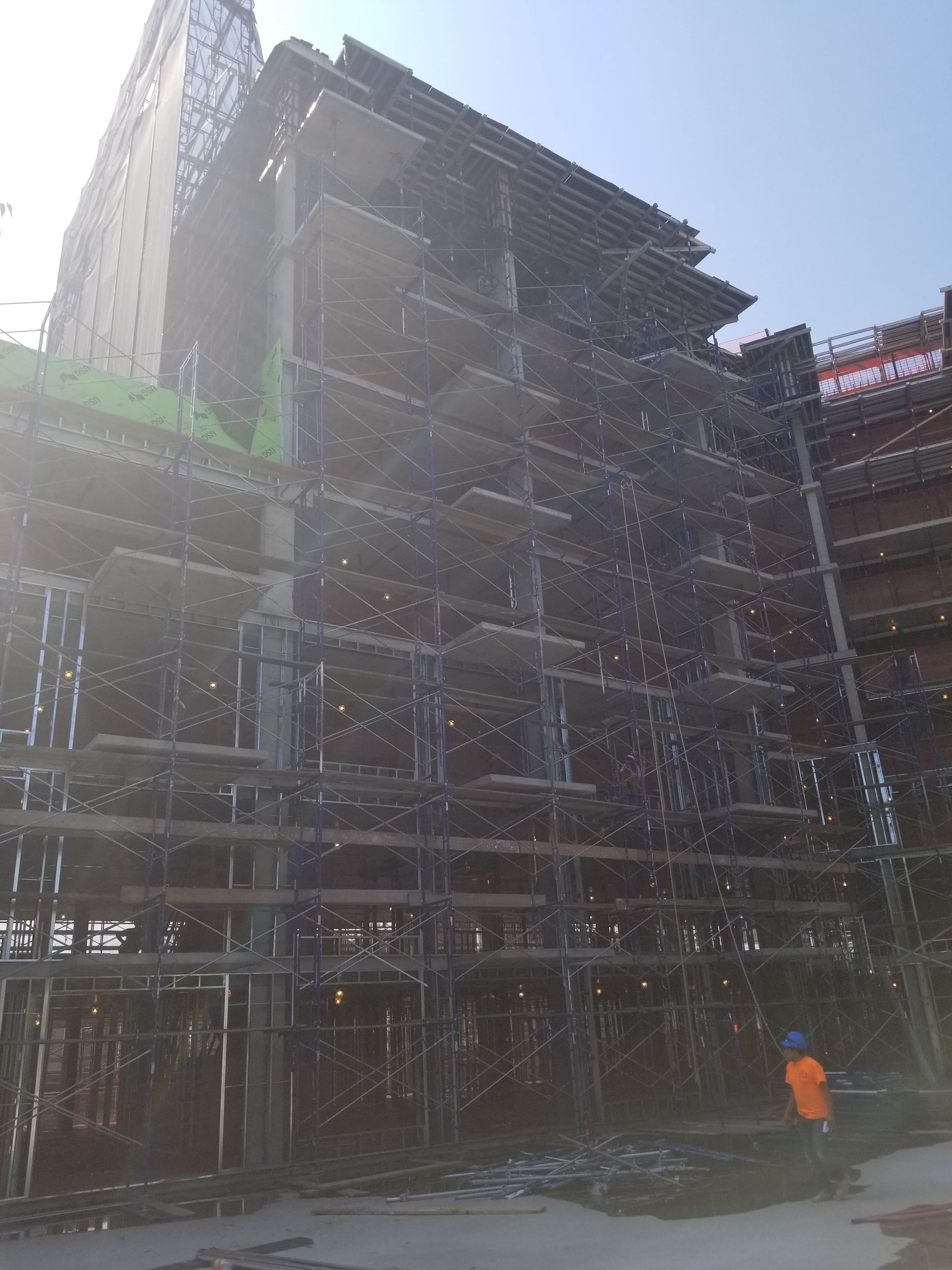 Construction site: multi-story building frame with scaffolding; worker in orange vest.