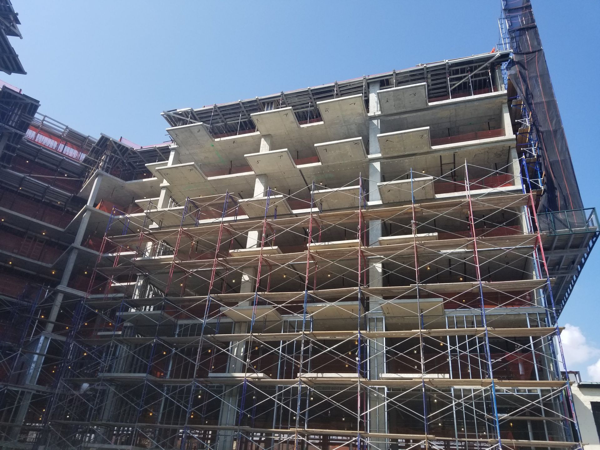 A multi-story building under construction with exposed concrete floors, scaffolding, and a blue sky backdrop.