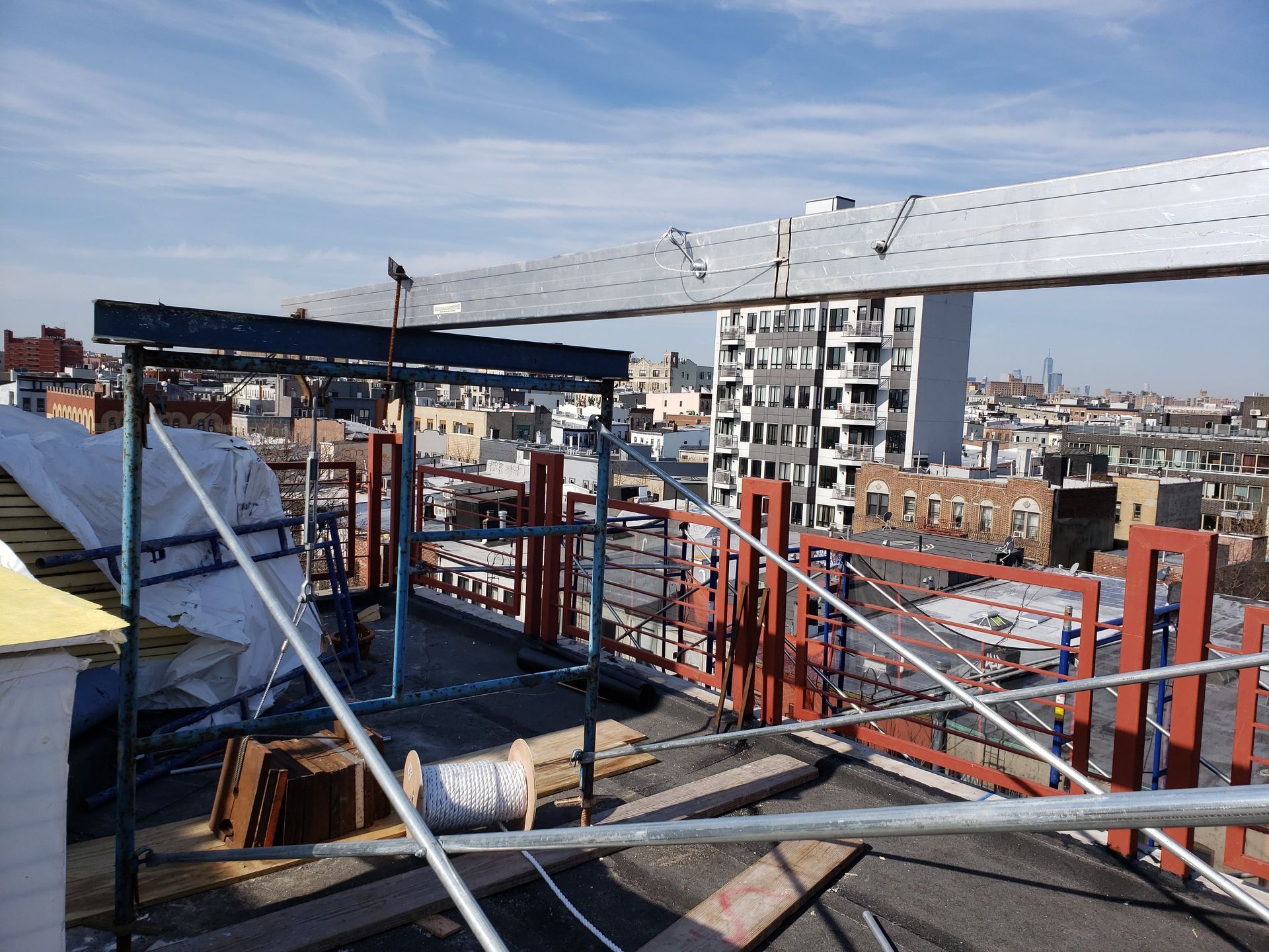 Rooftop construction site with scaffolding and cityscape background. Sunny day with a bright blue sky.