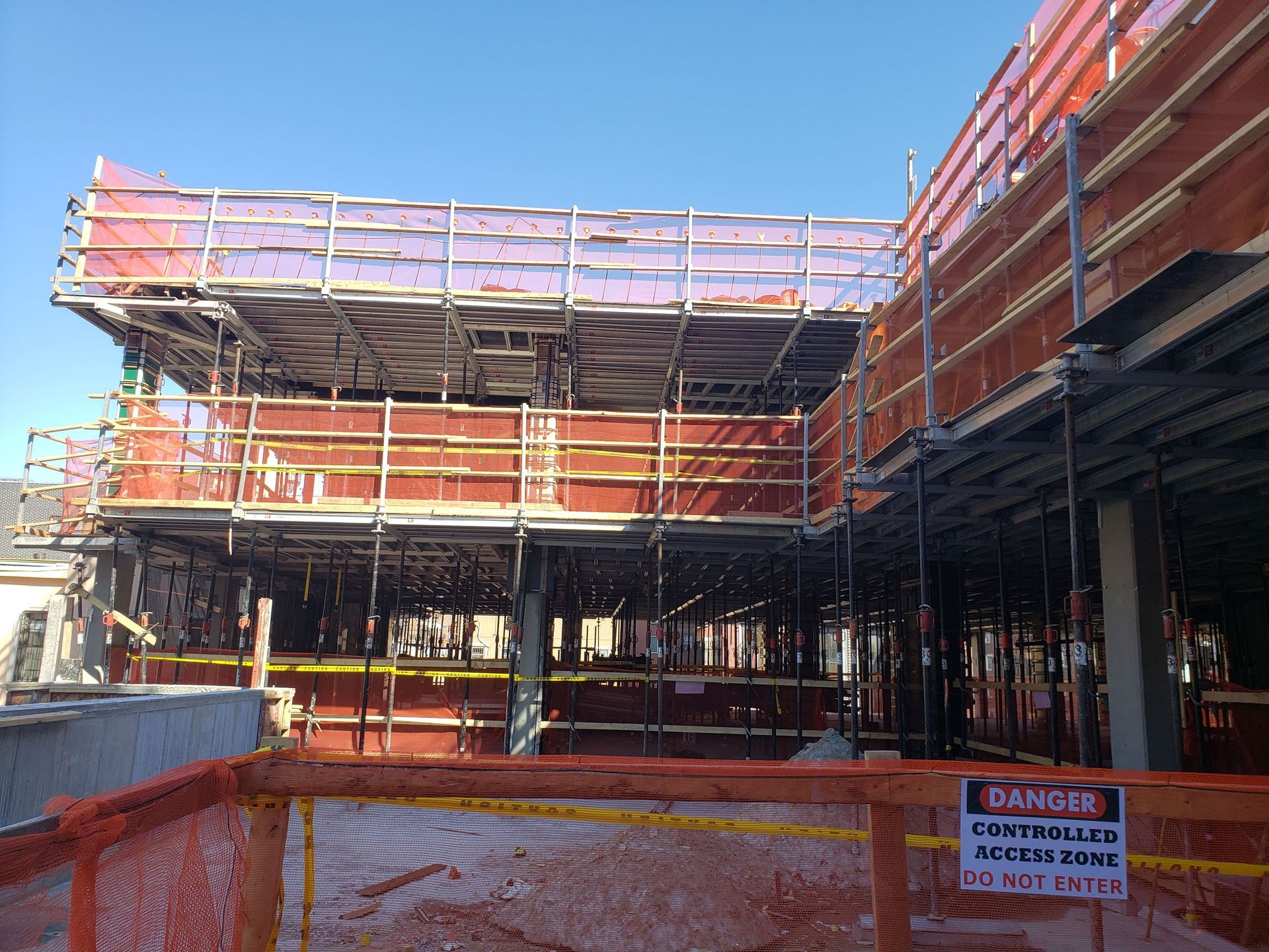 Construction site with scaffolding and orange safety netting against a blue sky.