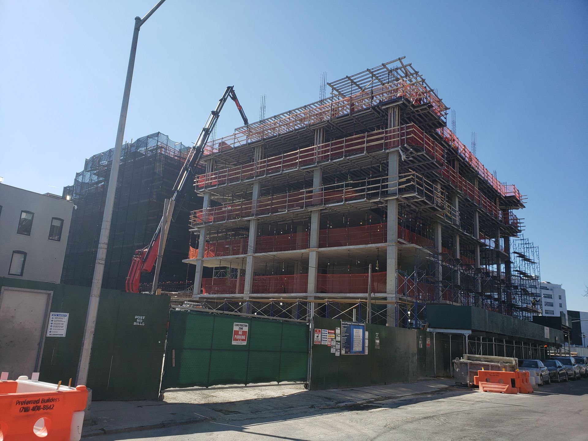 Construction site with a multi-story building frame, surrounded by fencing. Crane overhead.