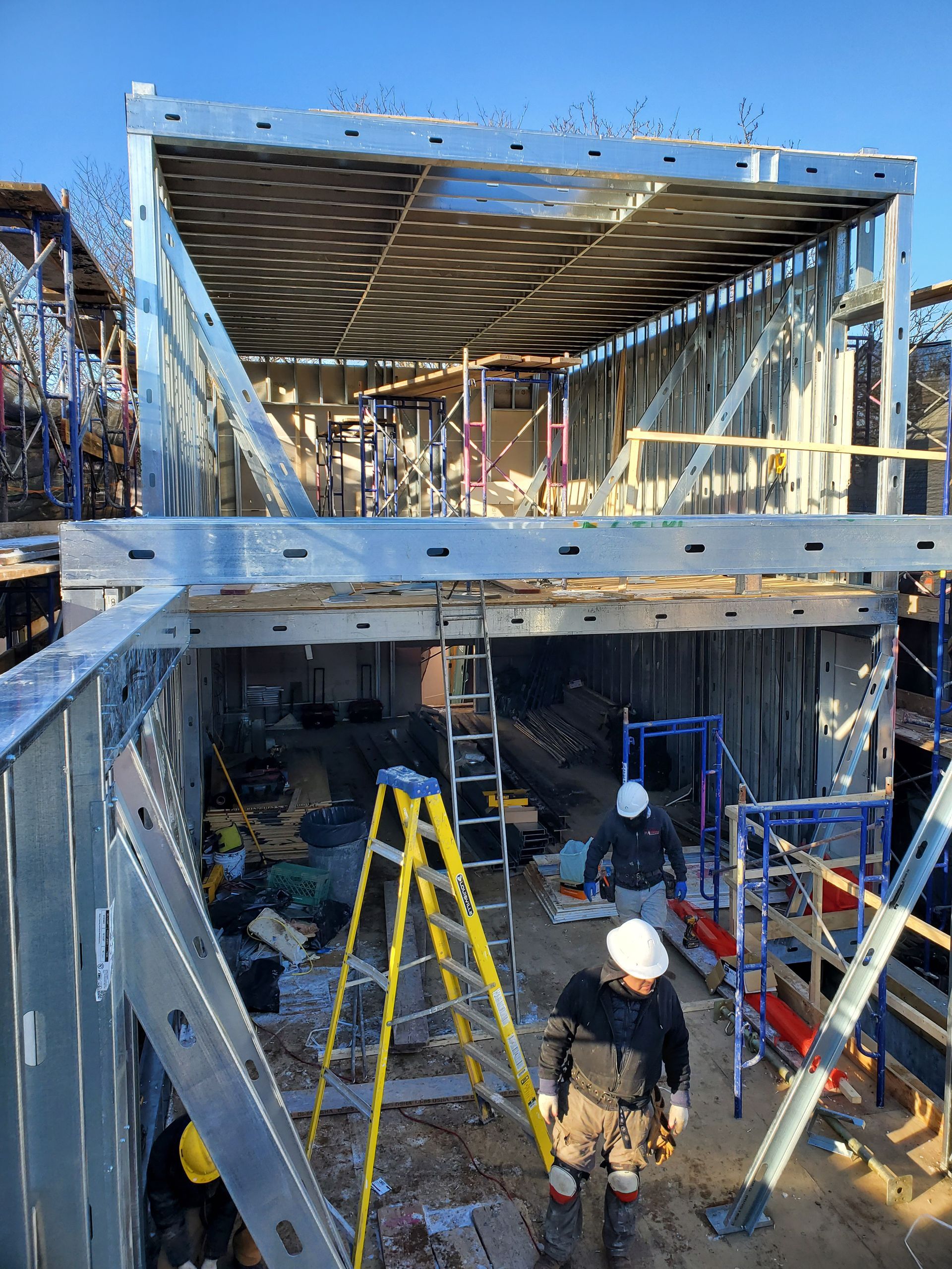 Construction of a building with steel framing. Workers on site, using ladders and scaffolding.