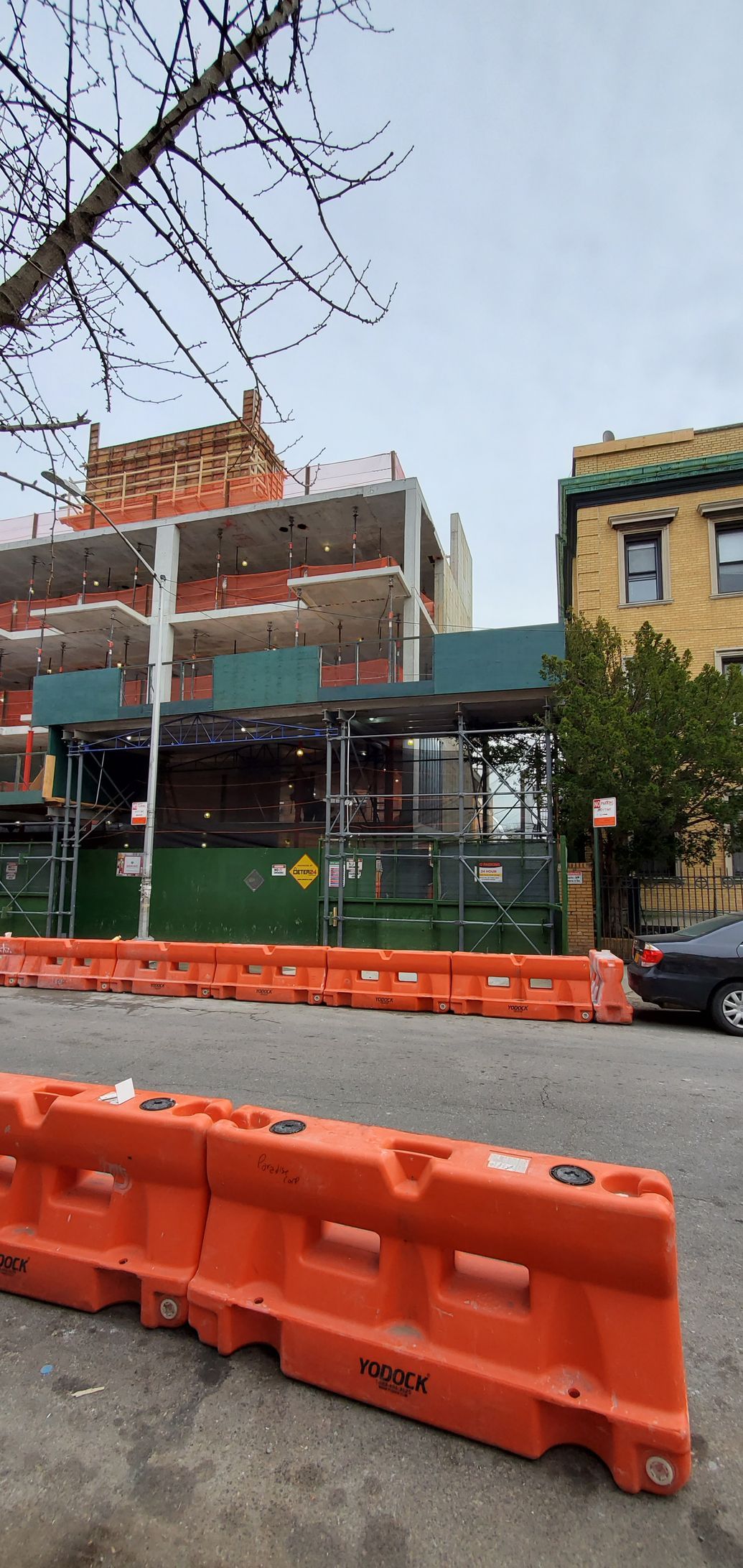 Construction site with orange barriers, building under construction and a building with windows. Cloudy day.