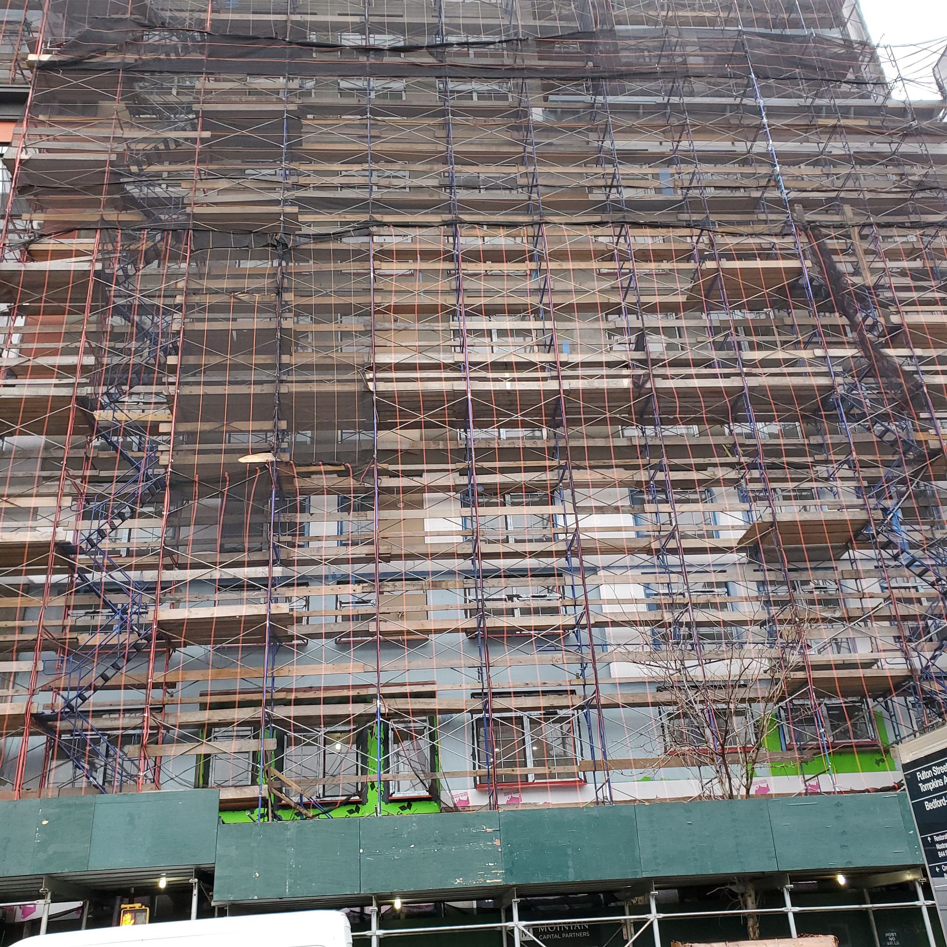 Building facade covered in scaffolding for construction. Green and white trim visible.