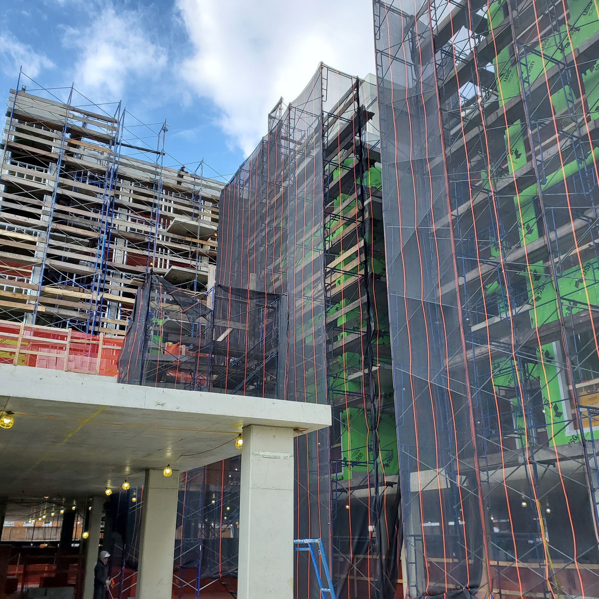 Building under construction with scaffolding and safety netting, cloudy sky background.