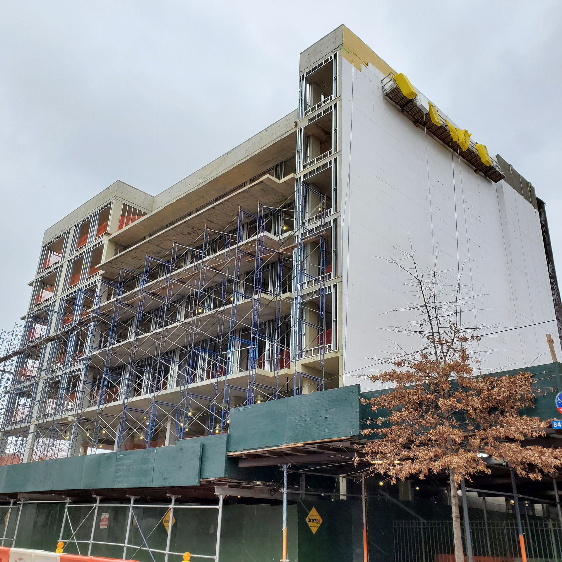 Building under construction, scaffolding wraps the facade. White and tan exterior with a green fence.
