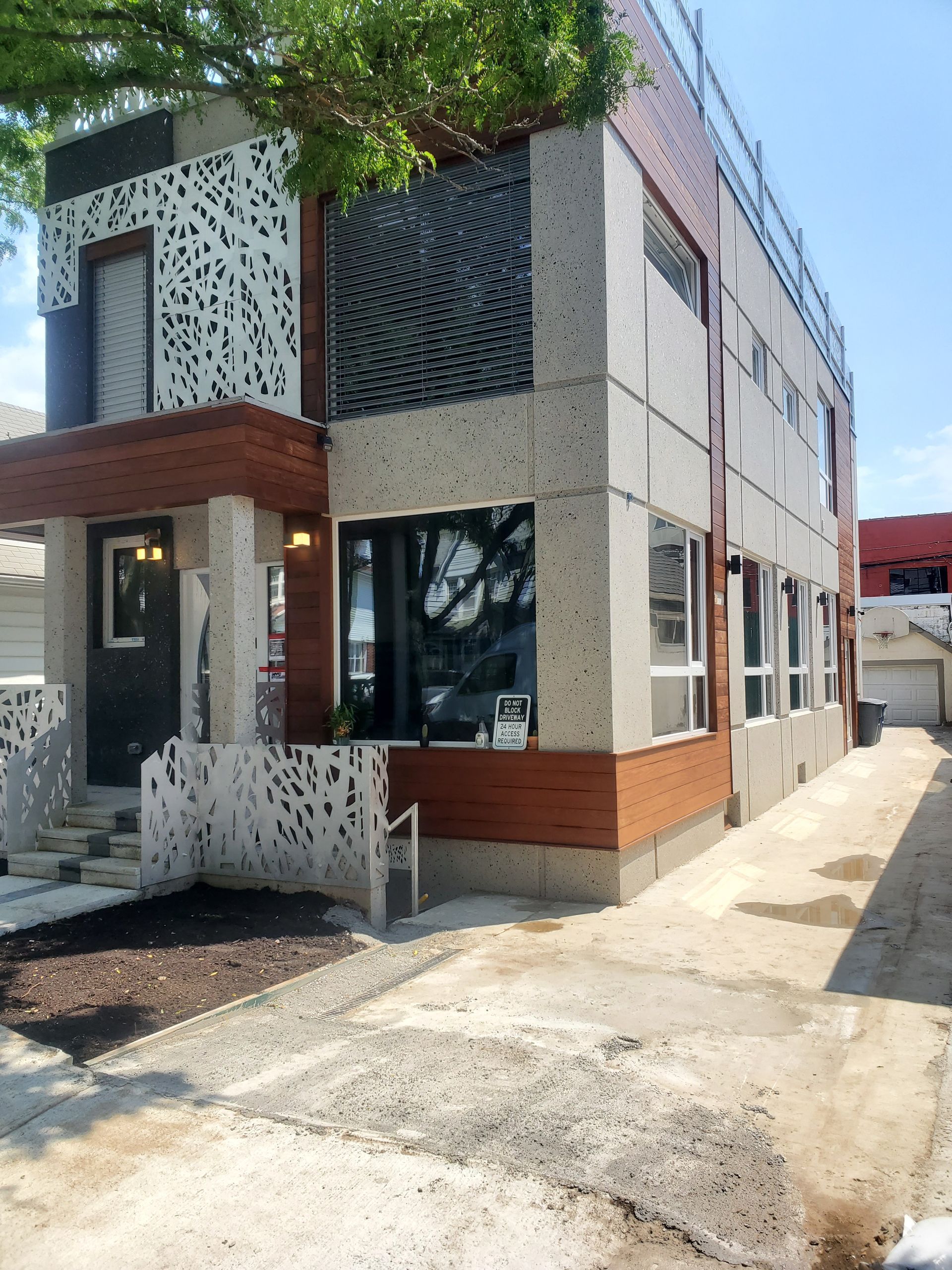 Modern two-story building with patterned facade and wooden accents, concrete driveway.