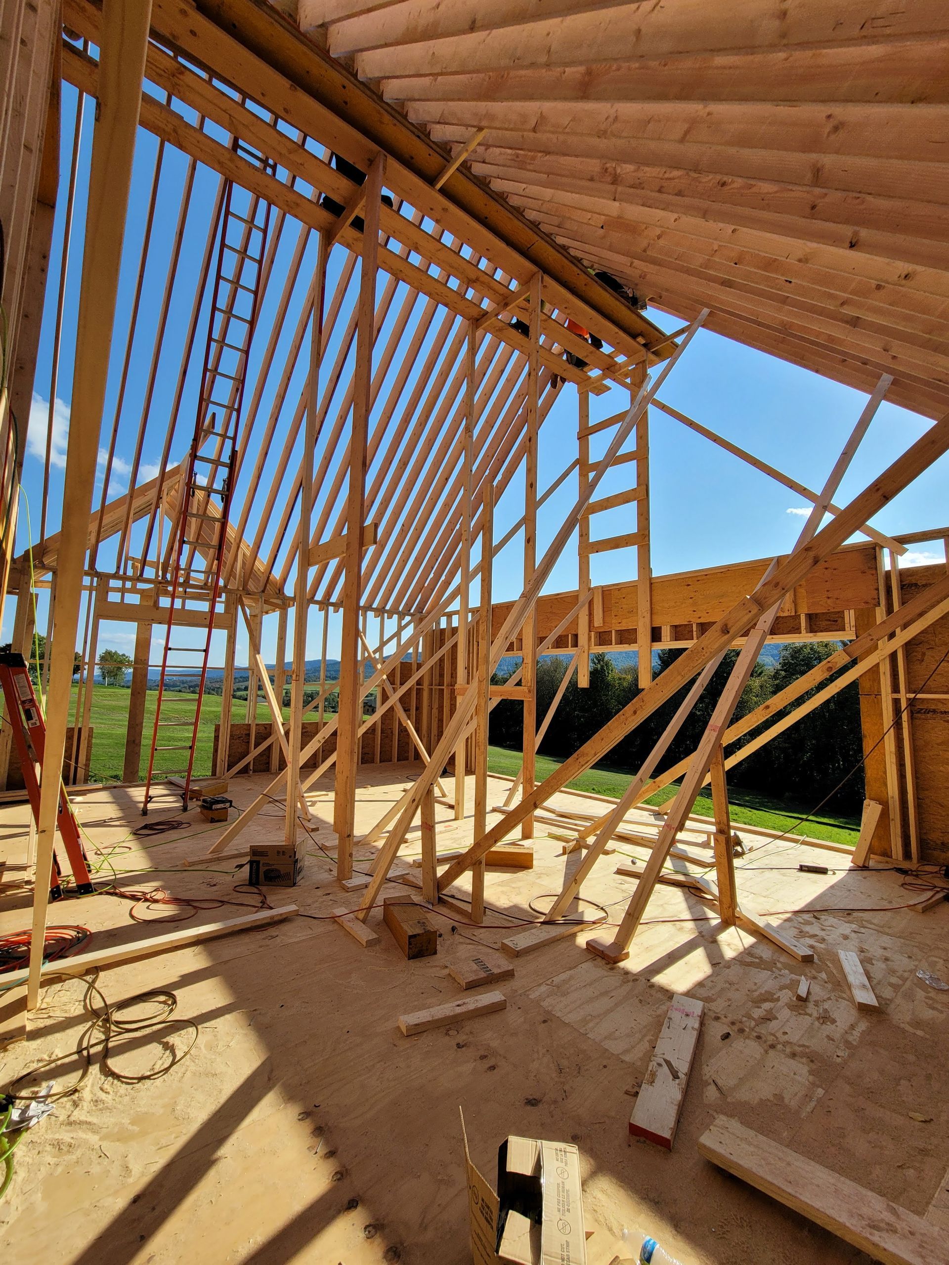 Interior view of a building under construction, showing wooden framework and exposed rafters. Blue sky visible.