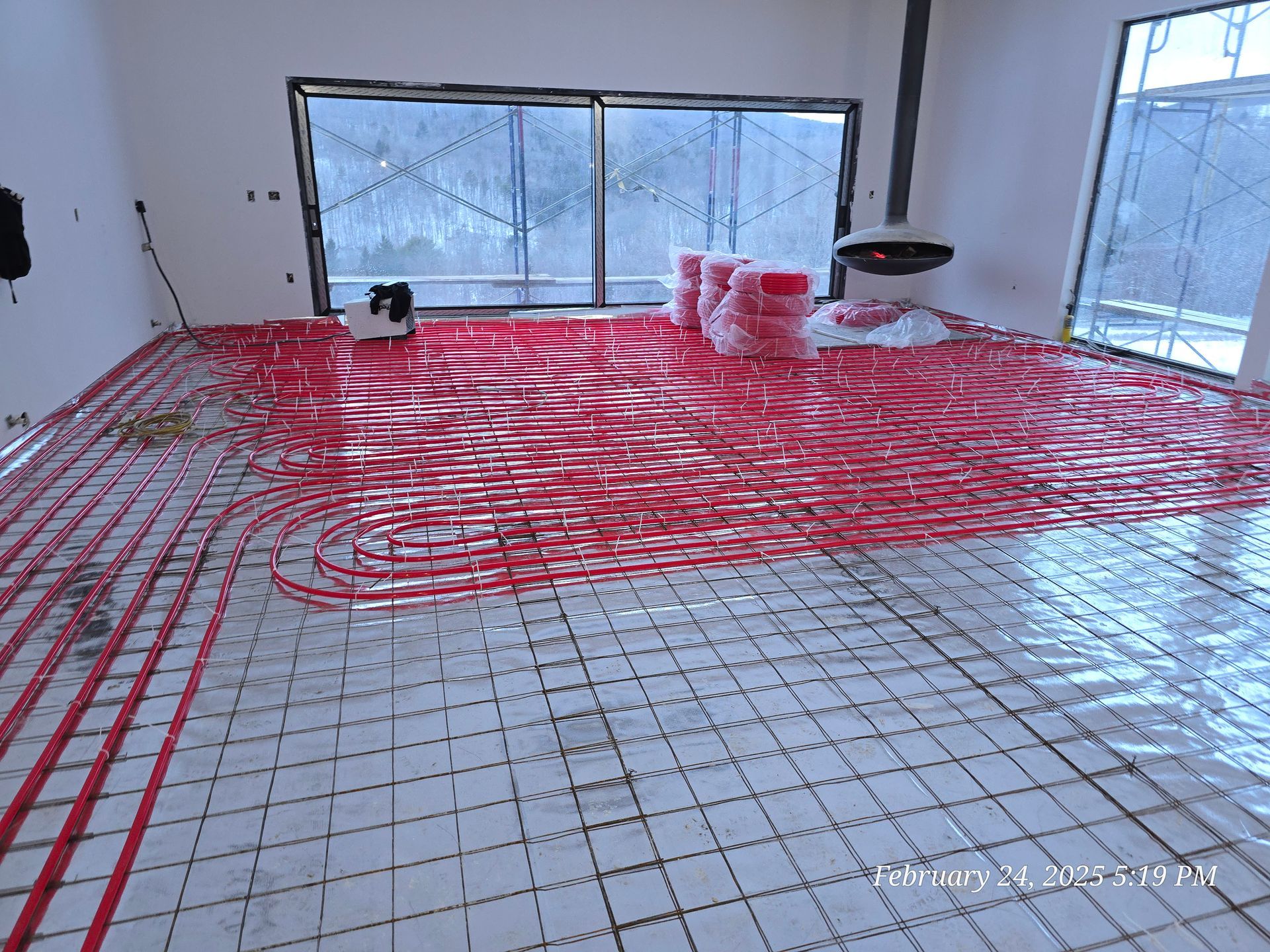 Red radiant floor heating pipes laid out on a grid in a room with windows.
