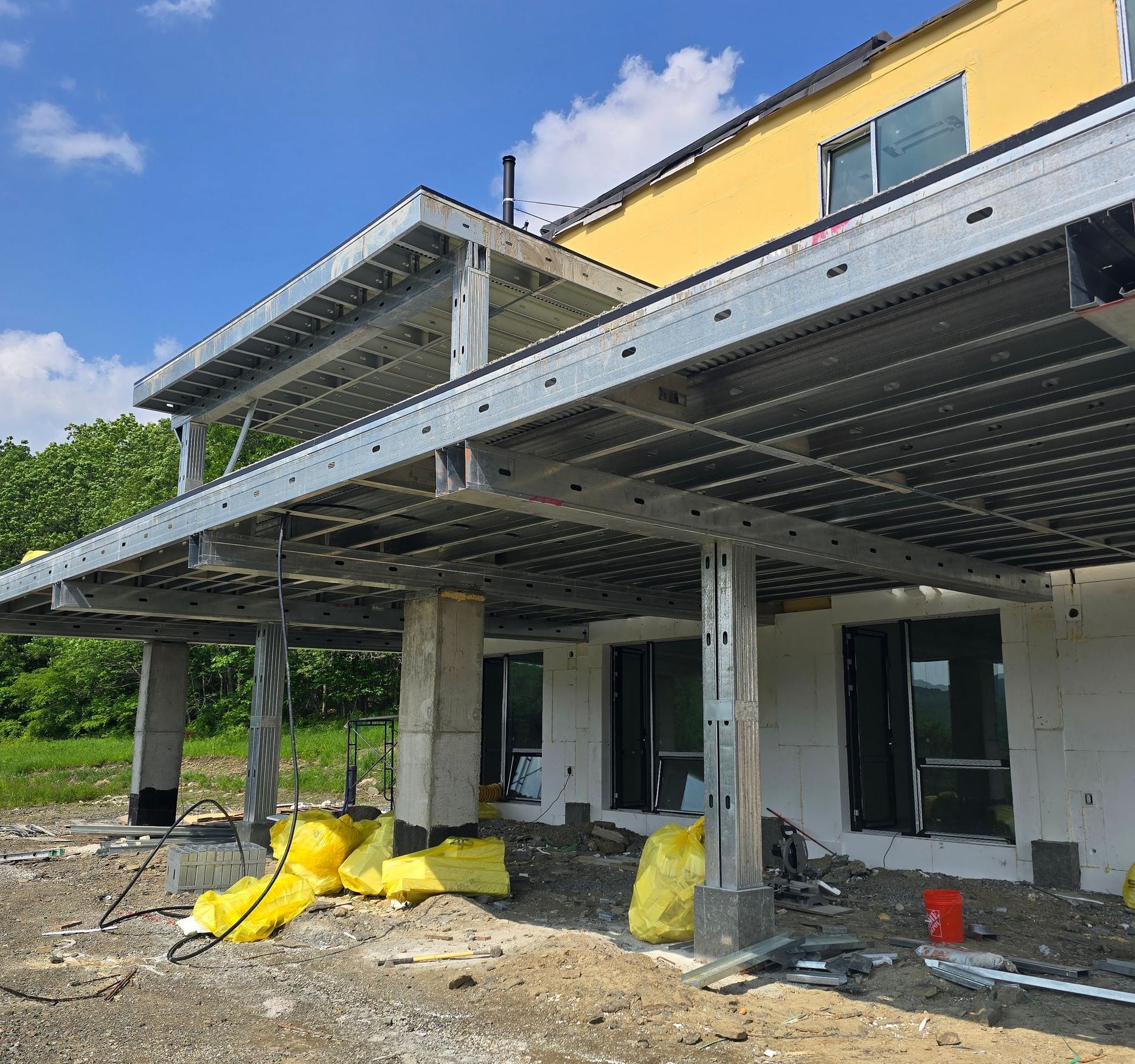 Construction of a two-story deck with a yellow building, and concrete columns. Steel frame supports the deck.