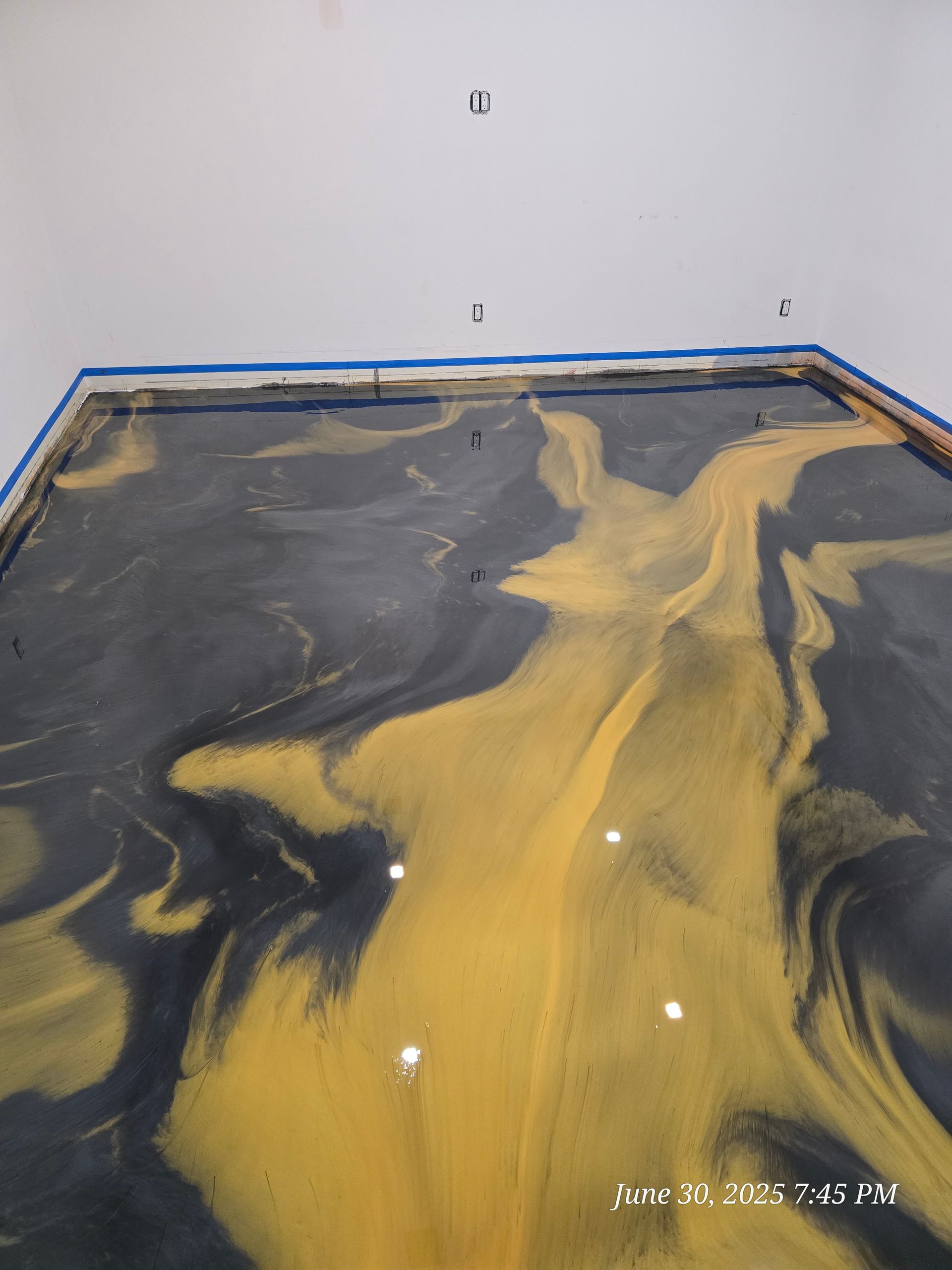 Black and gold swirled epoxy floor with light fixtures, blue tape at the edges, against a white wall.