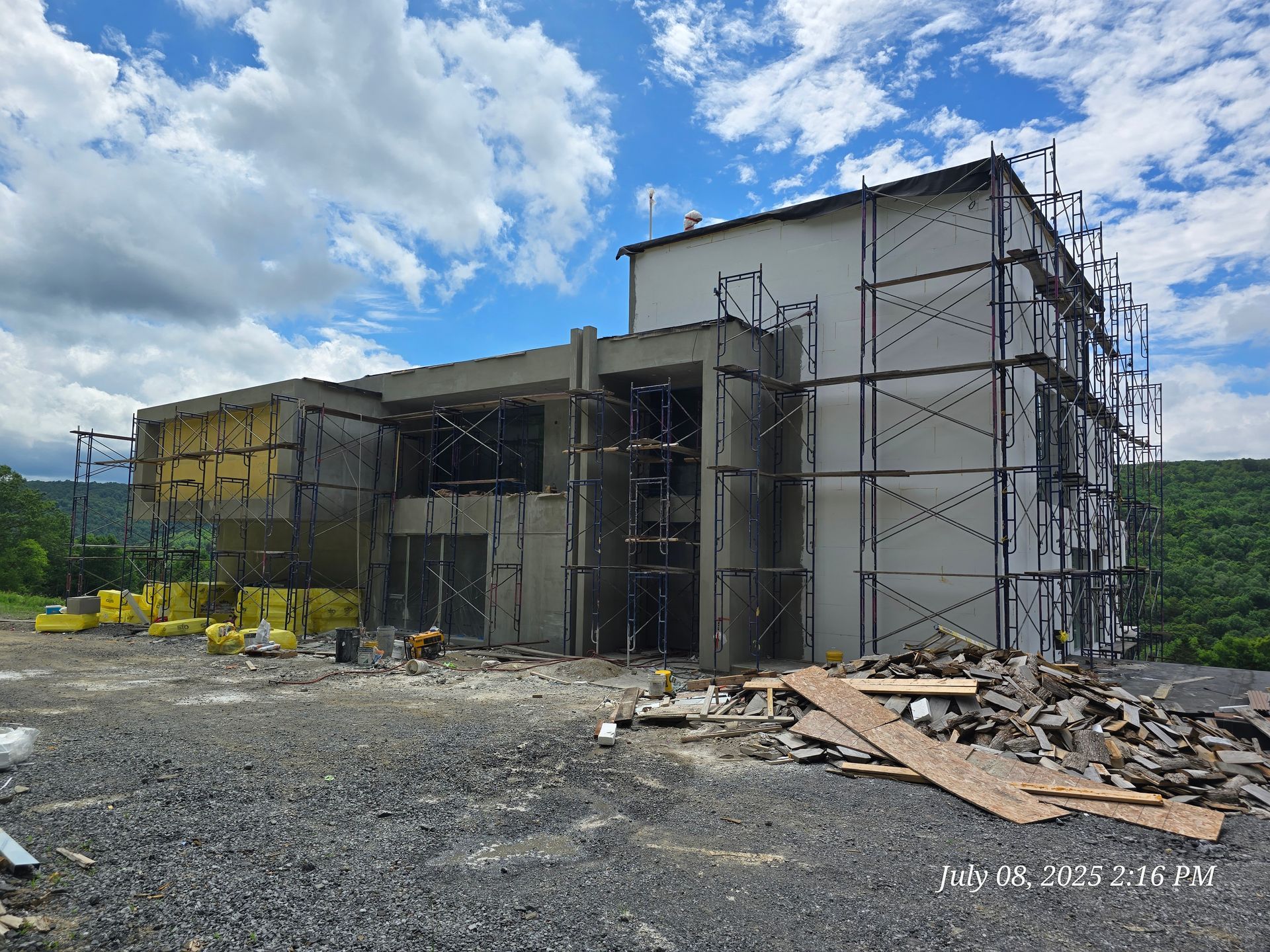 Building under construction, with scaffolding, unfinished exterior walls, and surrounding construction materials under a cloudy sky.