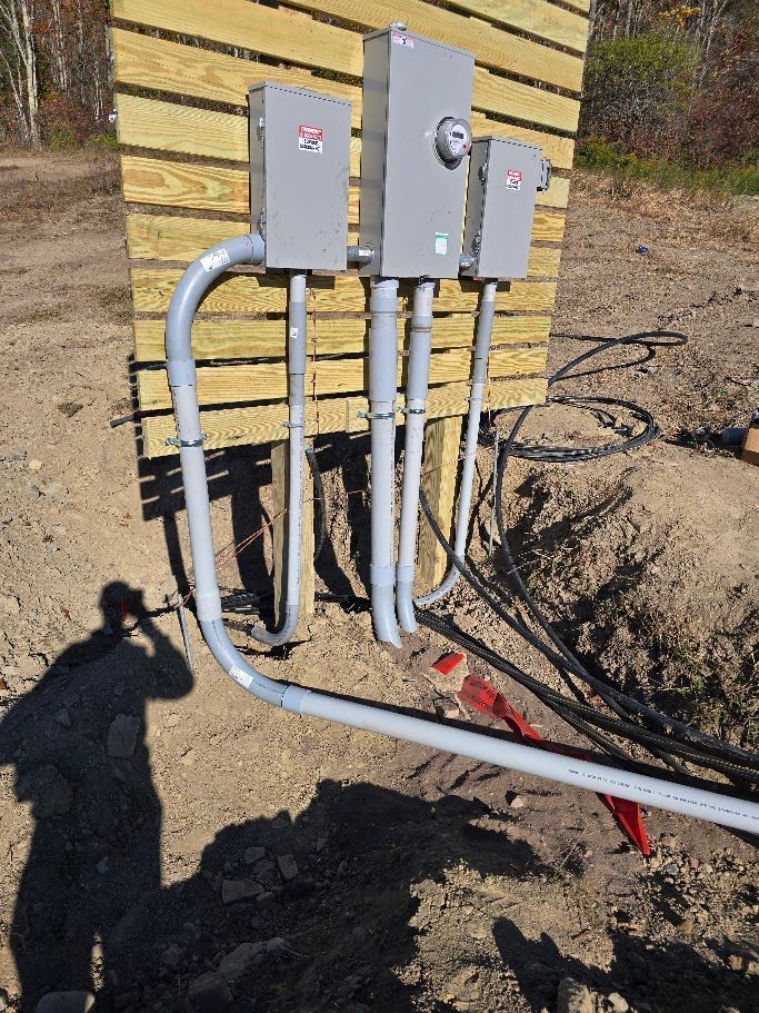 Electrical boxes on wooden post with conduit pipes, set in a dirt area.