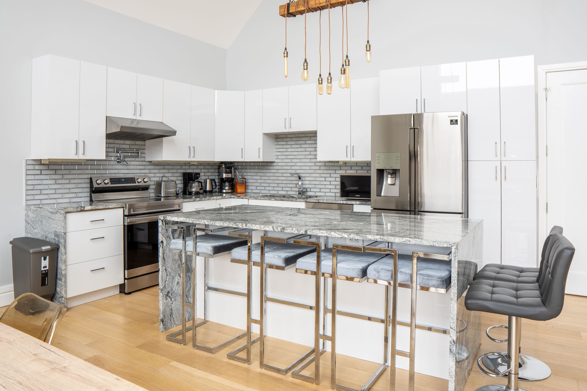 Modern white kitchen with stainless steel appliances, granite island, and bar stools.