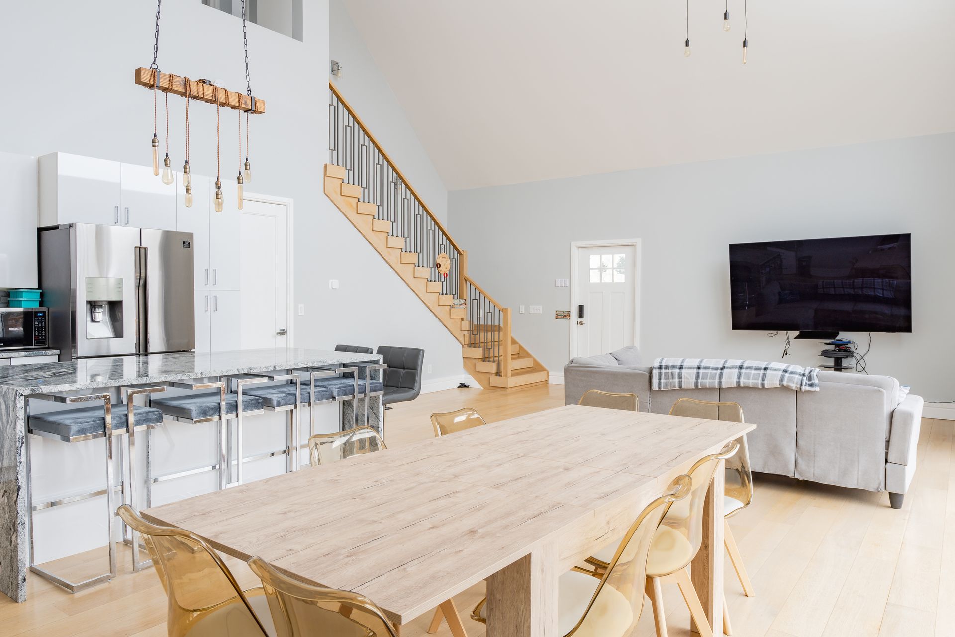Spacious open-concept living area with kitchen, dining, and living room. Light wood floors, white walls, and a staircase.