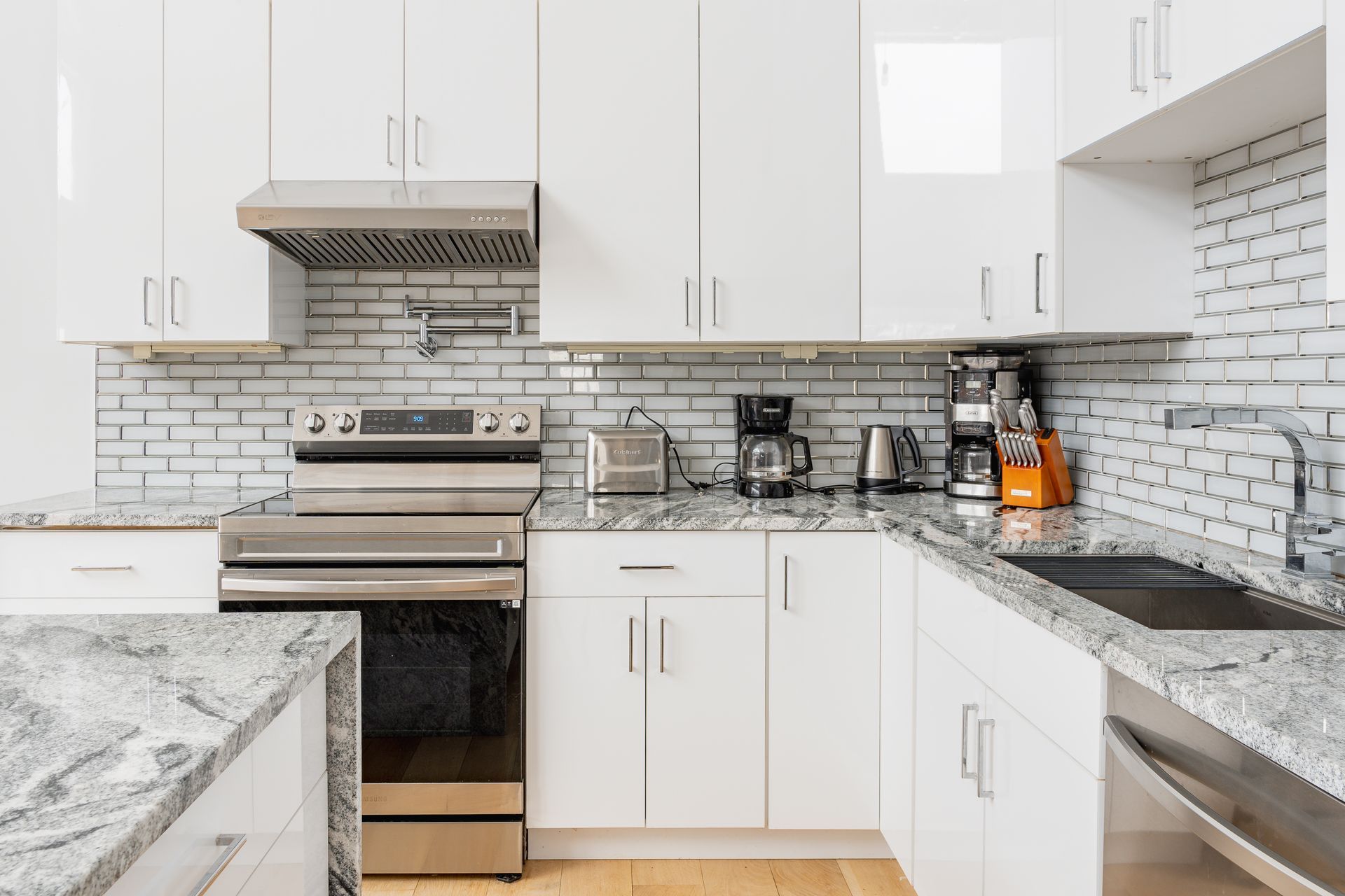 White kitchen with stainless steel appliances, granite countertops, and subway tile backsplash.