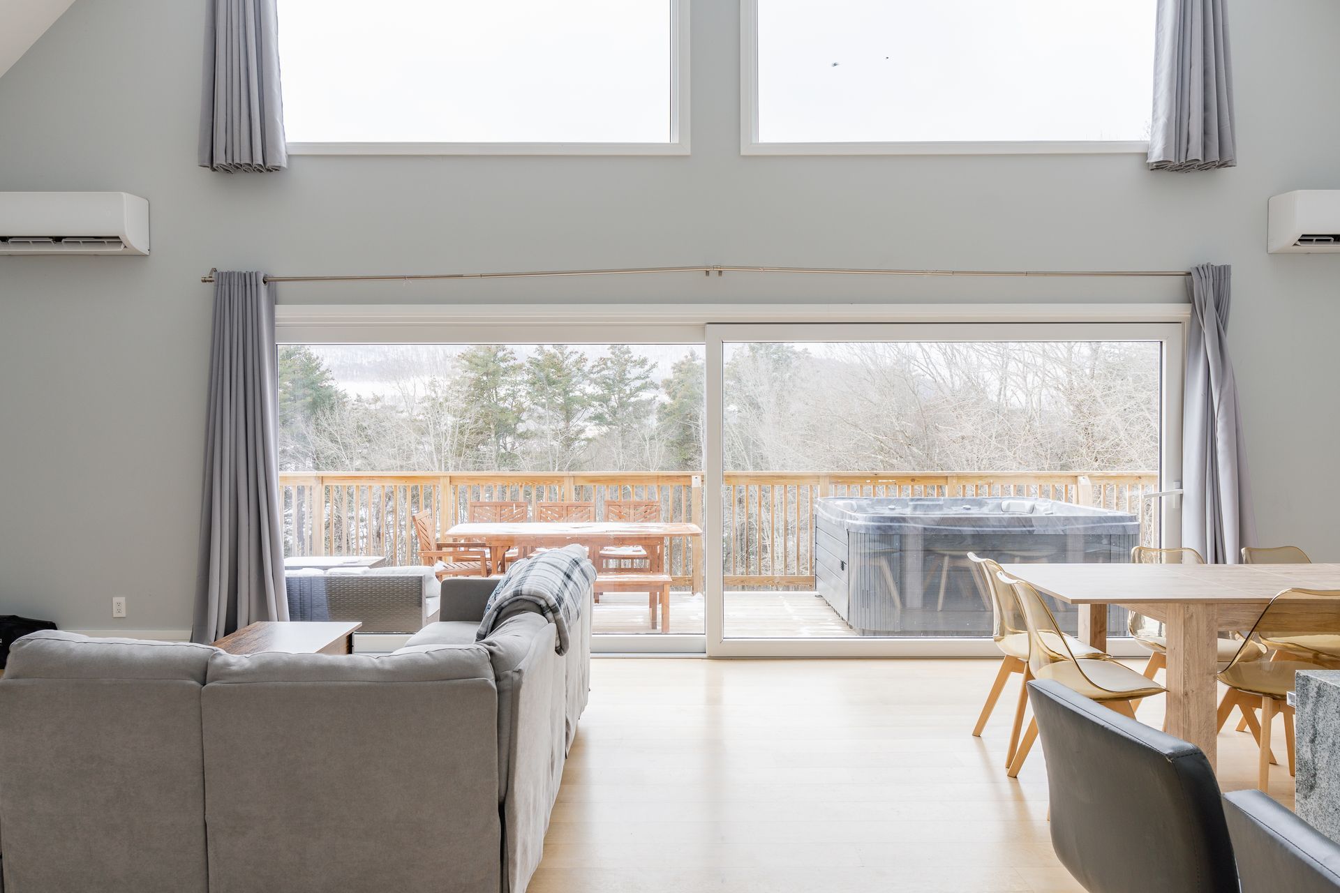 Spacious living room with large sliding doors leading to a deck with a hot tub and forest view.