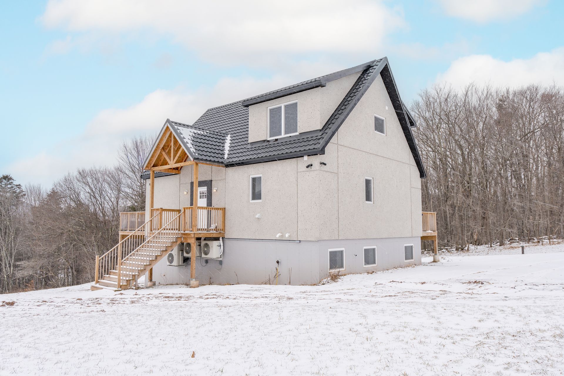 Two-story white house with black roof, wooden porch, and snow-covered ground.