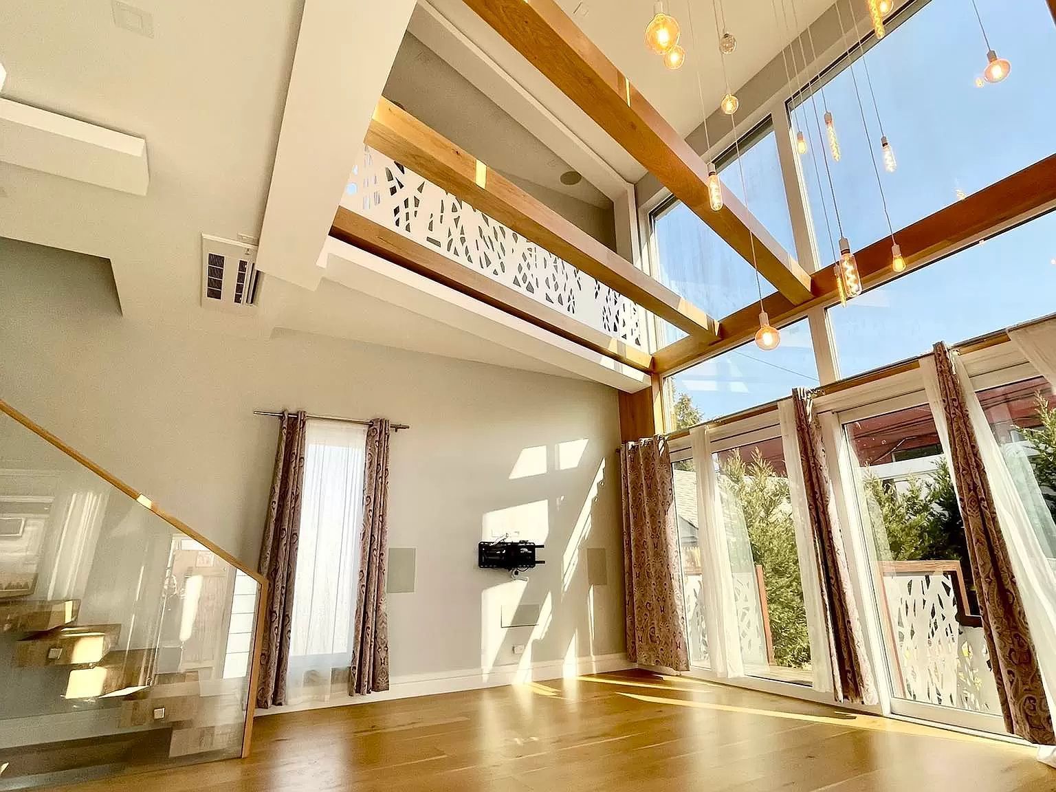 Spacious room with wooden beams, large windows, and hardwood floors. Sunlight streams through the windows.