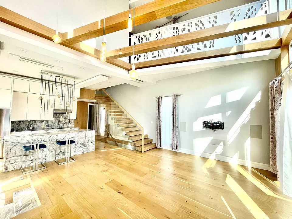 Spacious modern interior with high ceilings, kitchen island, wood floors, and staircase.
