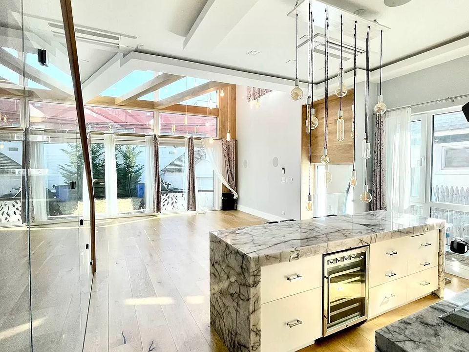 Modern kitchen with marble island, wine fridge, wood floor, and glass walls leading to a patio.