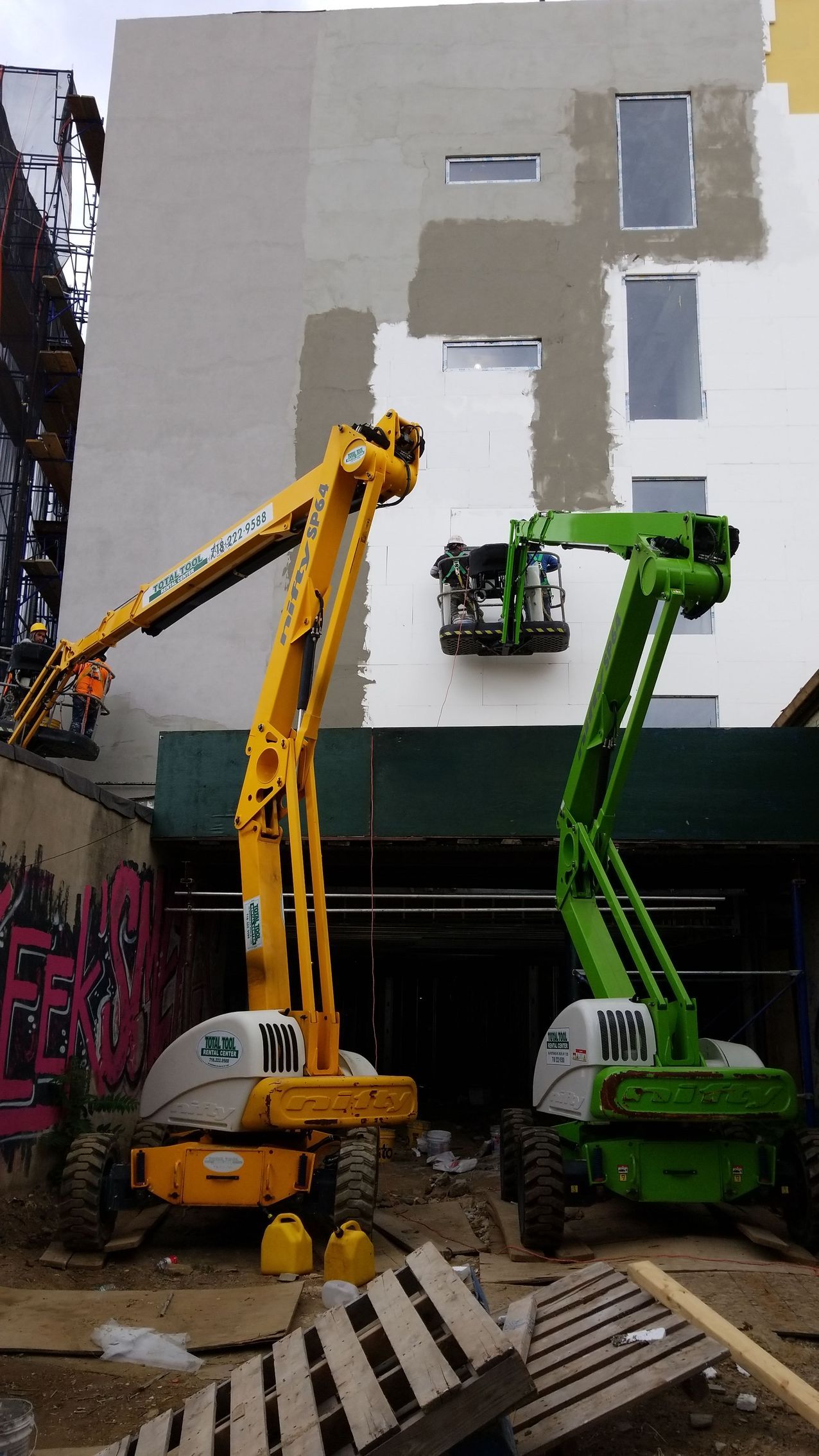 Yellow and green aerial lifts painting a building exterior. Construction site.