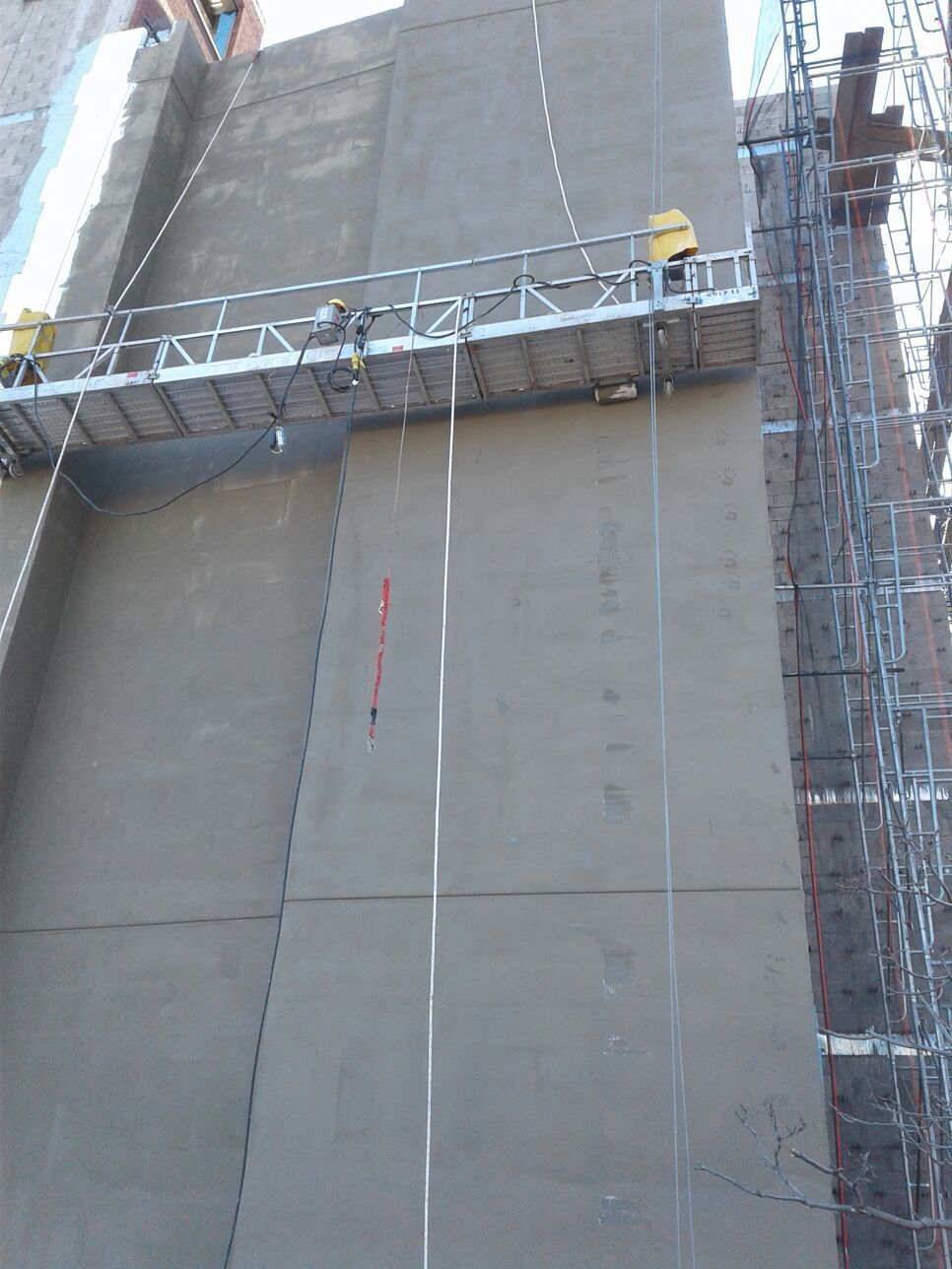 Workers on a suspended scaffold applying stucco to the exterior of a tall building.