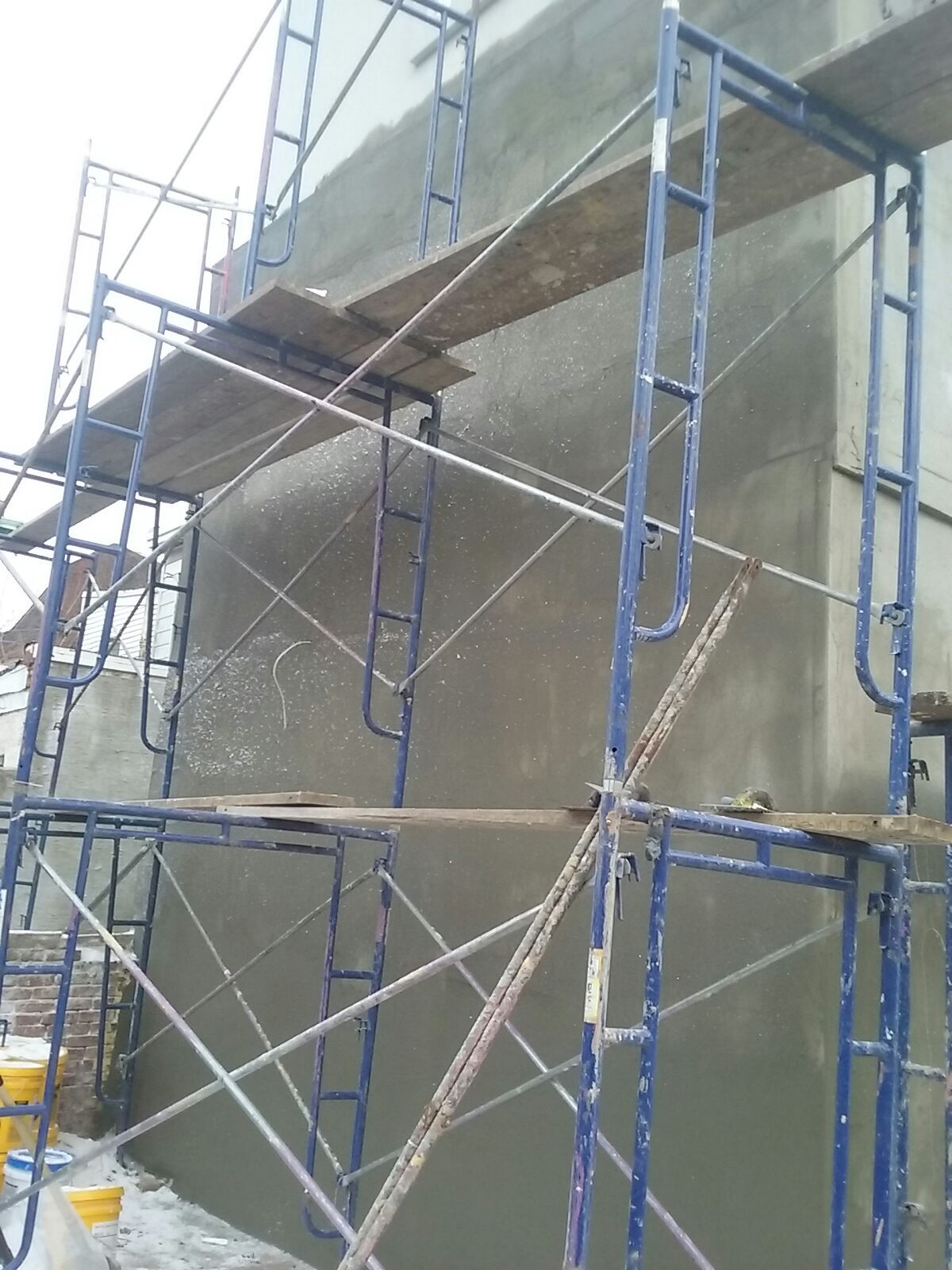 Scaffolding next to a concrete wall, with planks providing working platforms during construction.