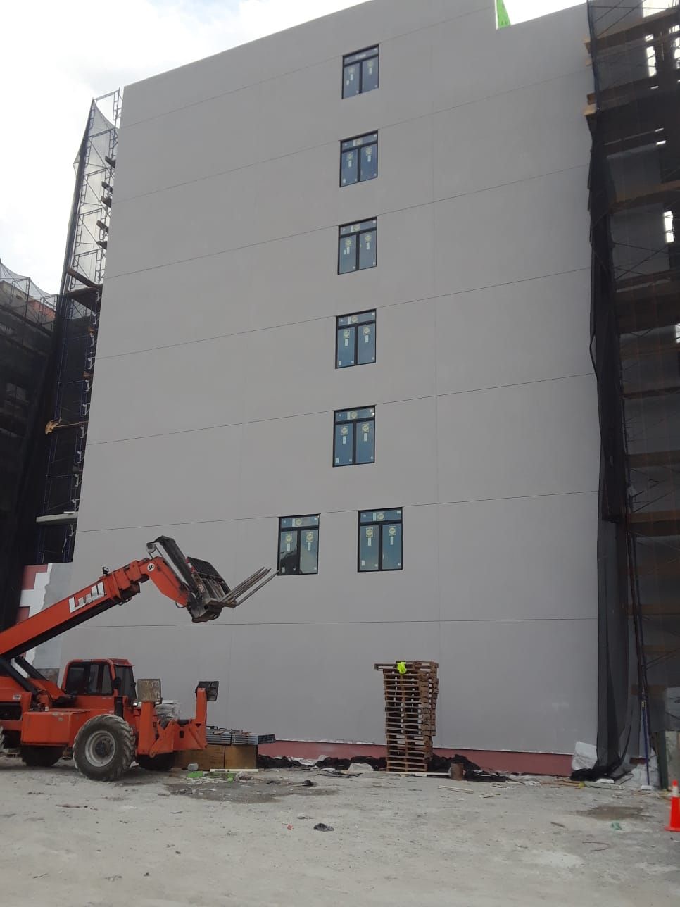A multi-story building under construction with windows, an orange forklift, and scaffolding.