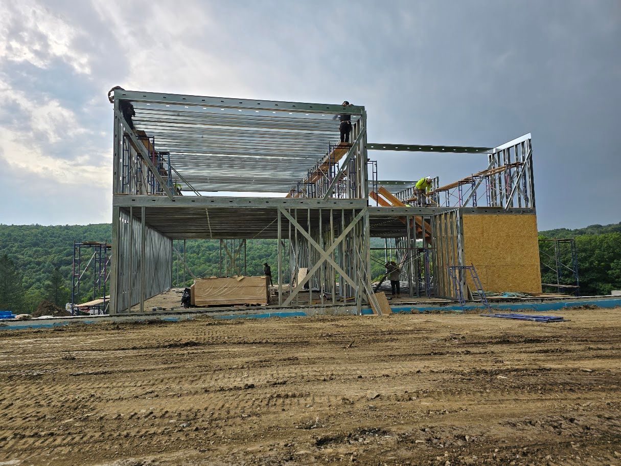 Construction site: Metal frame building partially constructed on a muddy lot, with workers visible.
