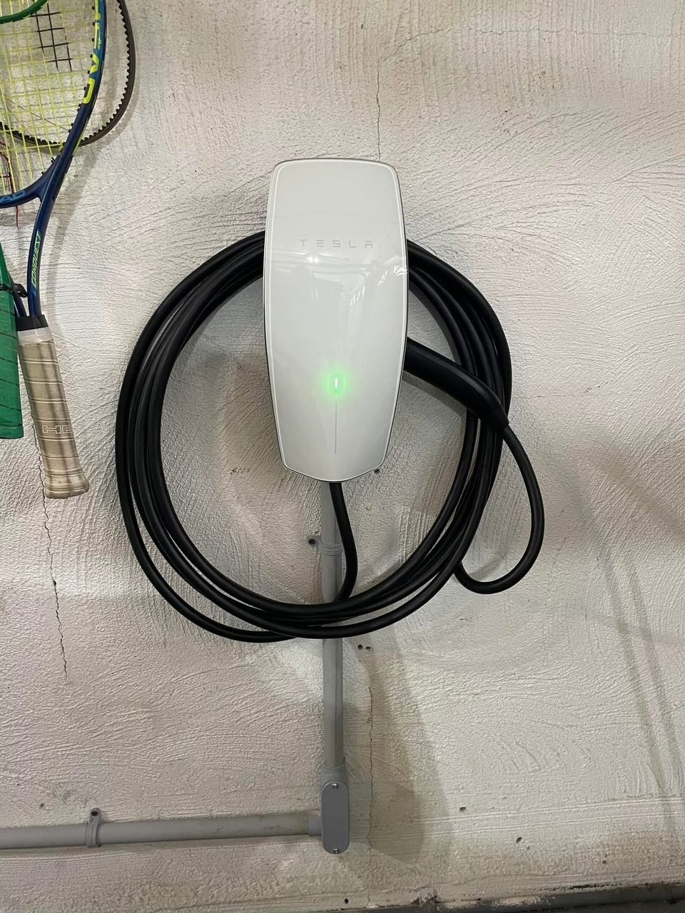 A tesla charger is hanging on a wall next to a badminton racket.