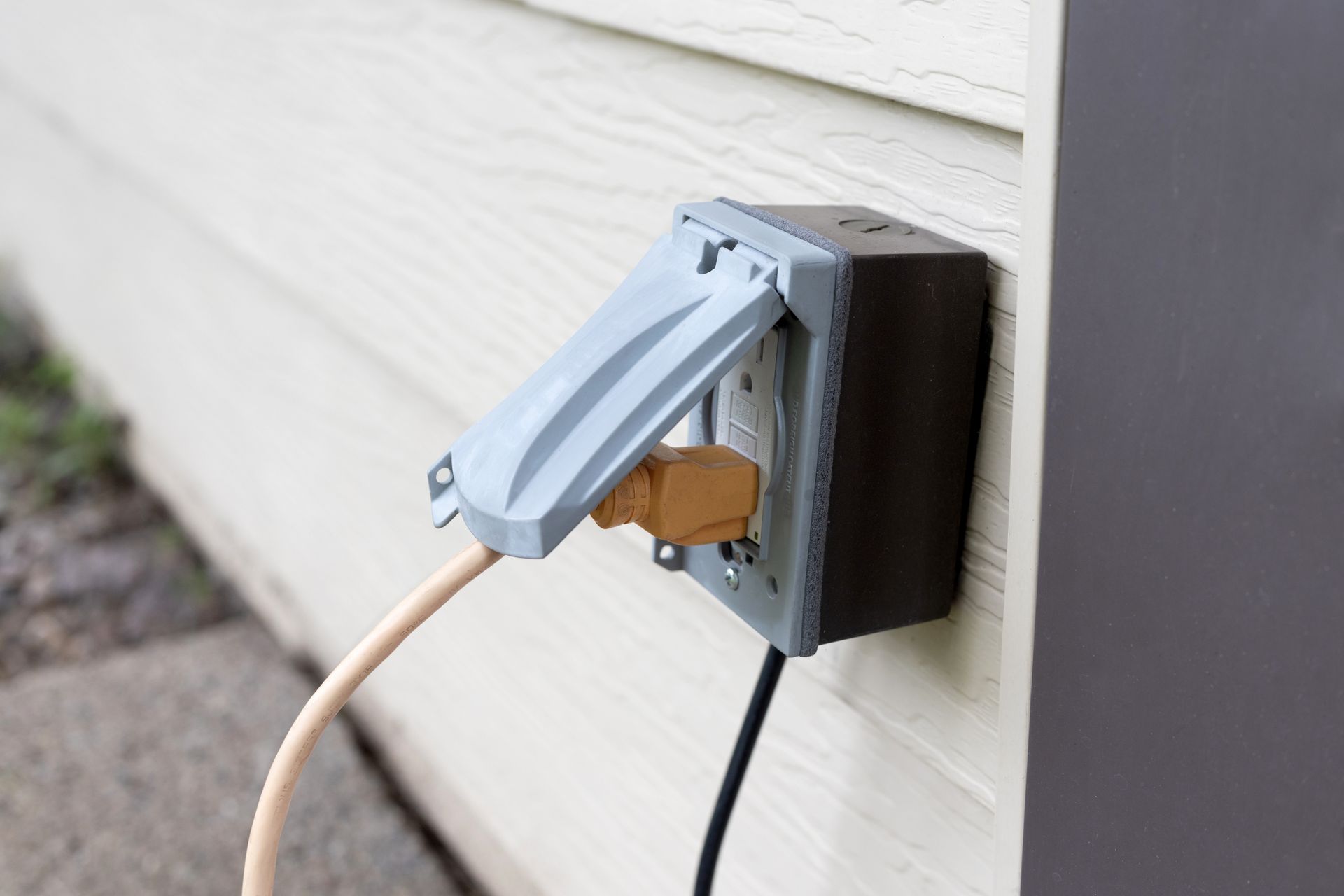 A power outlet on the side of a house with a cord plugged into it.