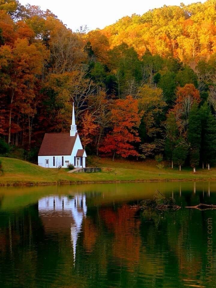 A small white church sits on the shore of a lake