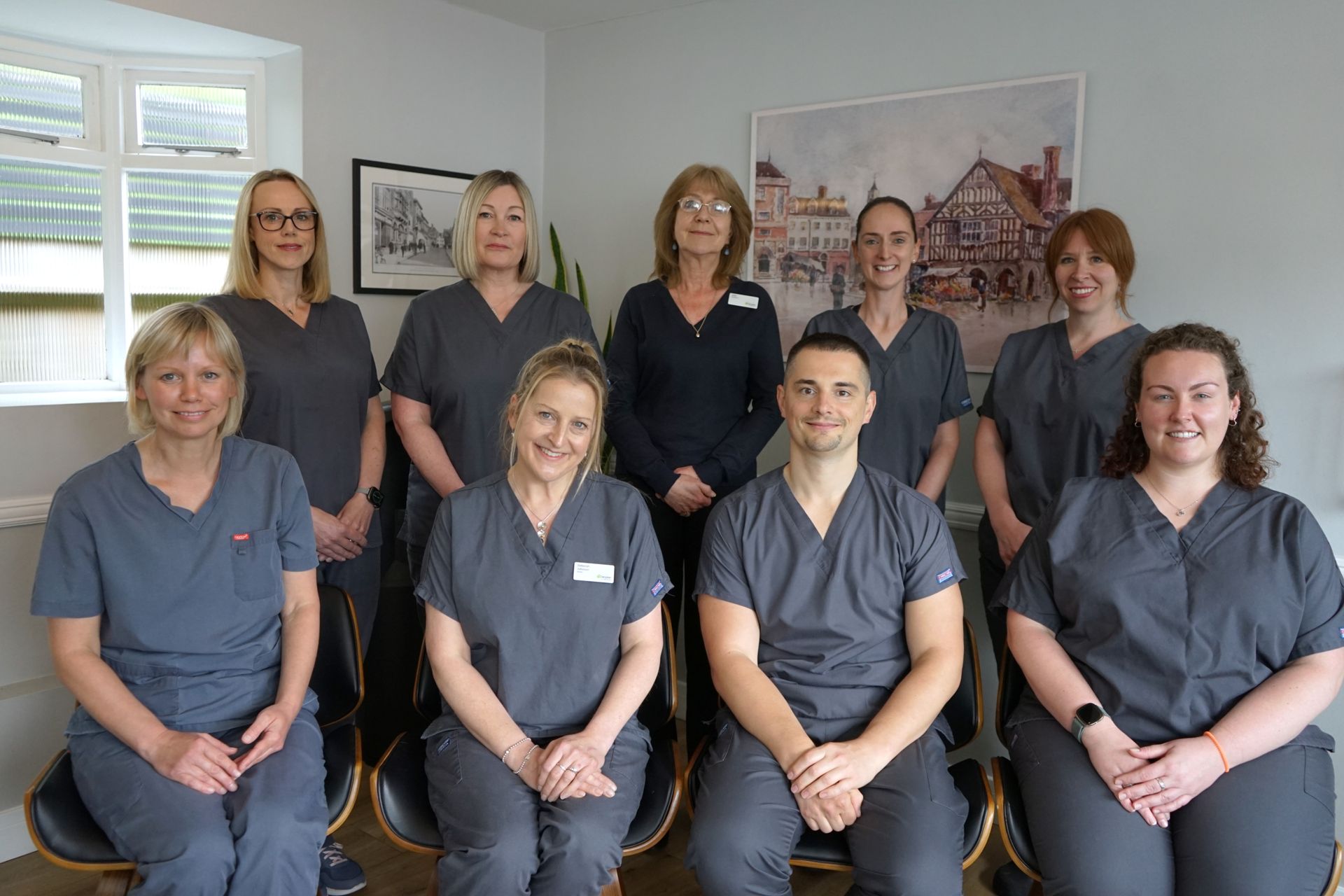 A group of smiling dental staff in gray scrubs, posing indoors.