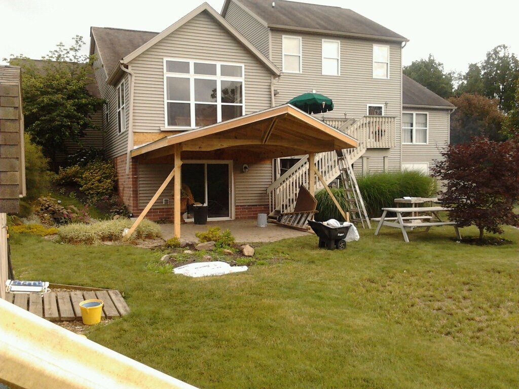 Backyard with house and patio under construction; wood canopy over door, green grass.