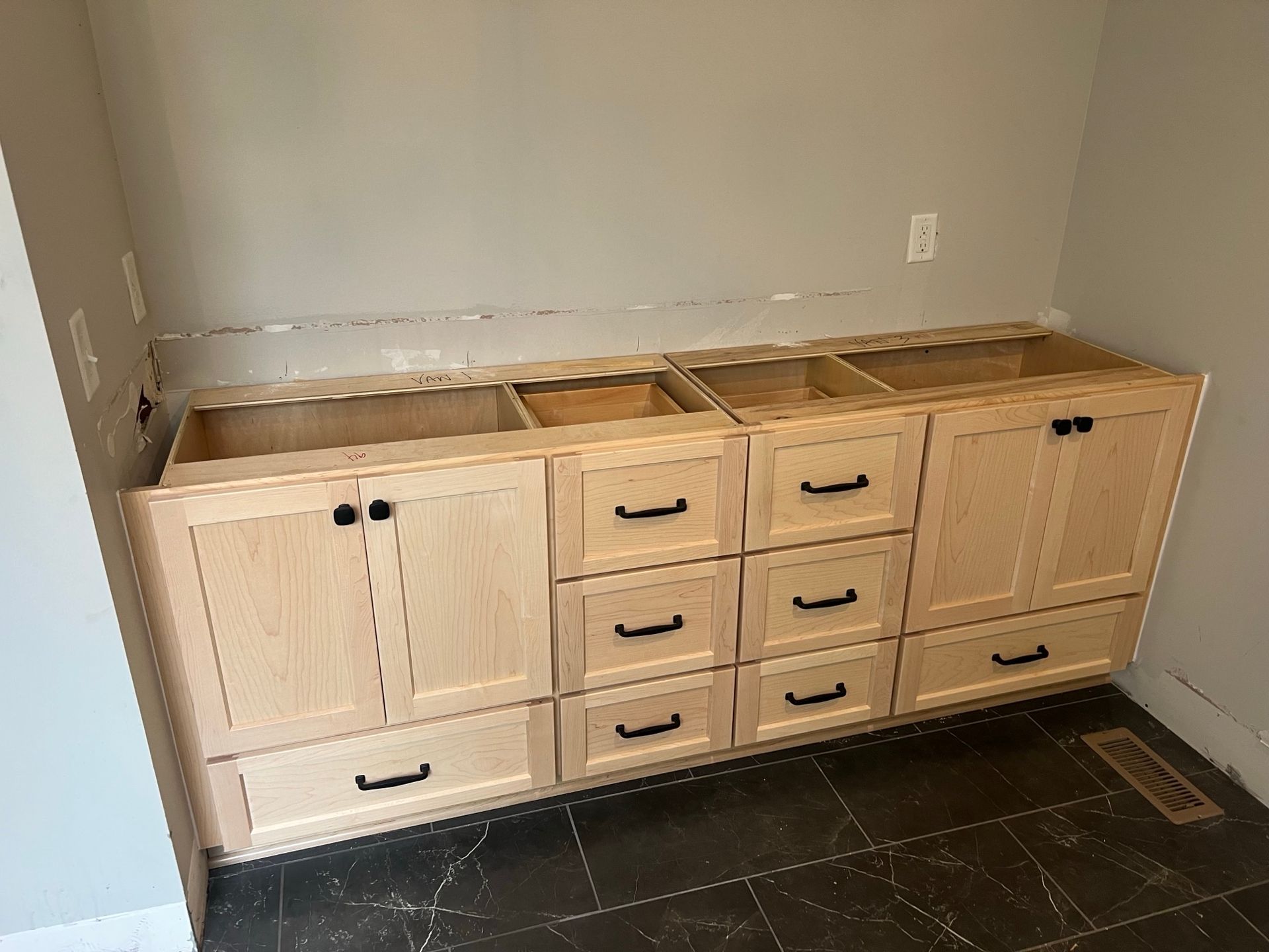Light wood bathroom vanity with drawers and cabinets, installed against a gray wall.