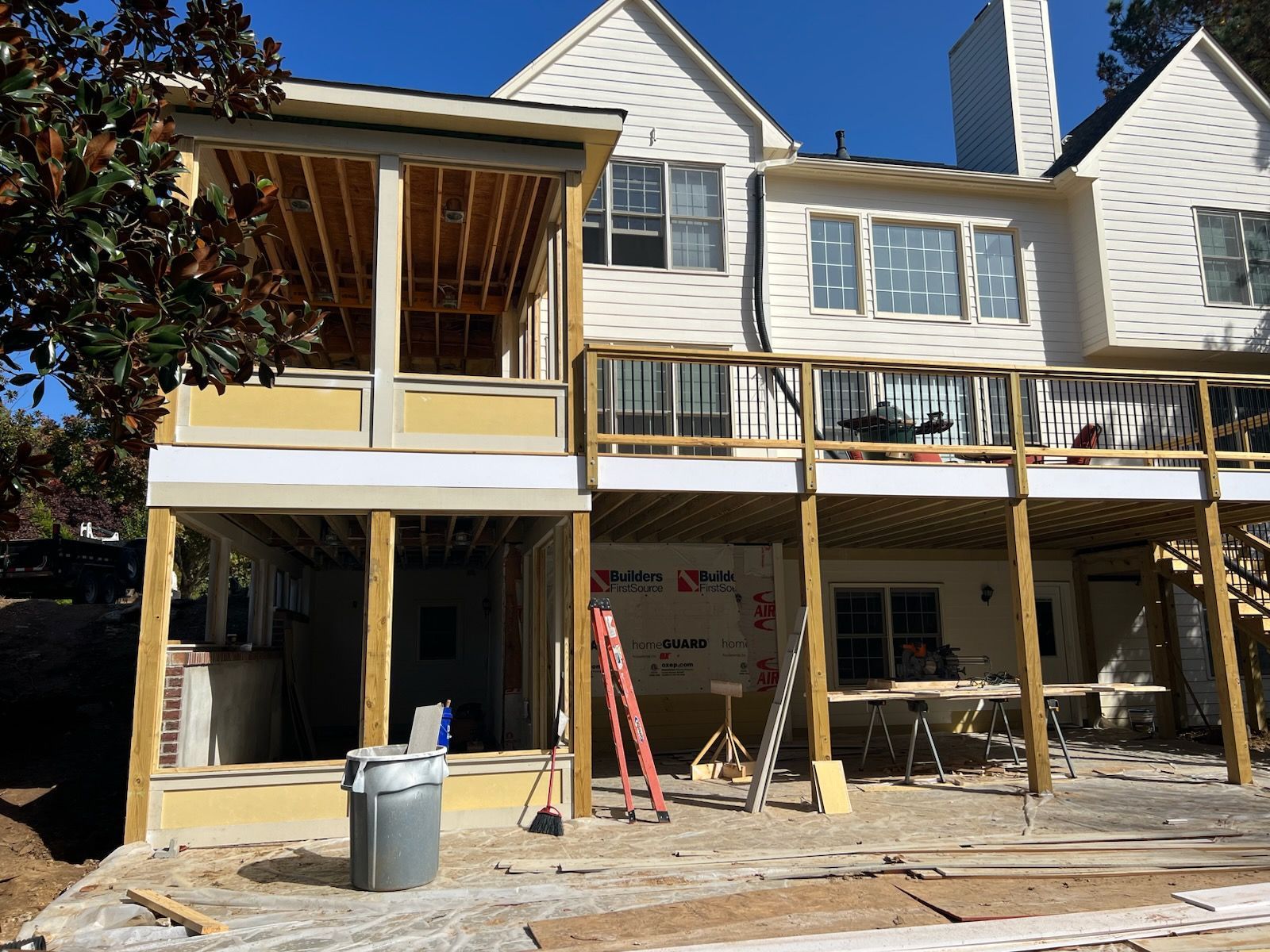 Two-story house with unfinished deck and sunroom construction; sunny day.