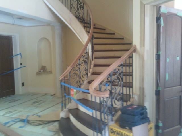 Curved staircase with wooden steps, ornate iron railing, and a light beige interior.