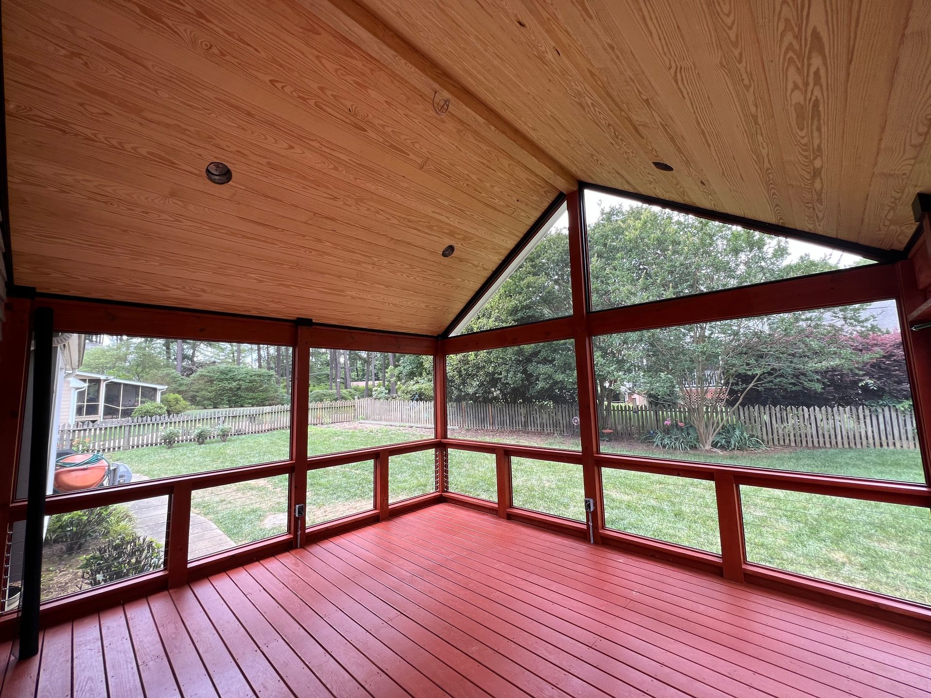 Screened-in porch with red wood floor and trim, wooden ceiling, and view of a green backyard.