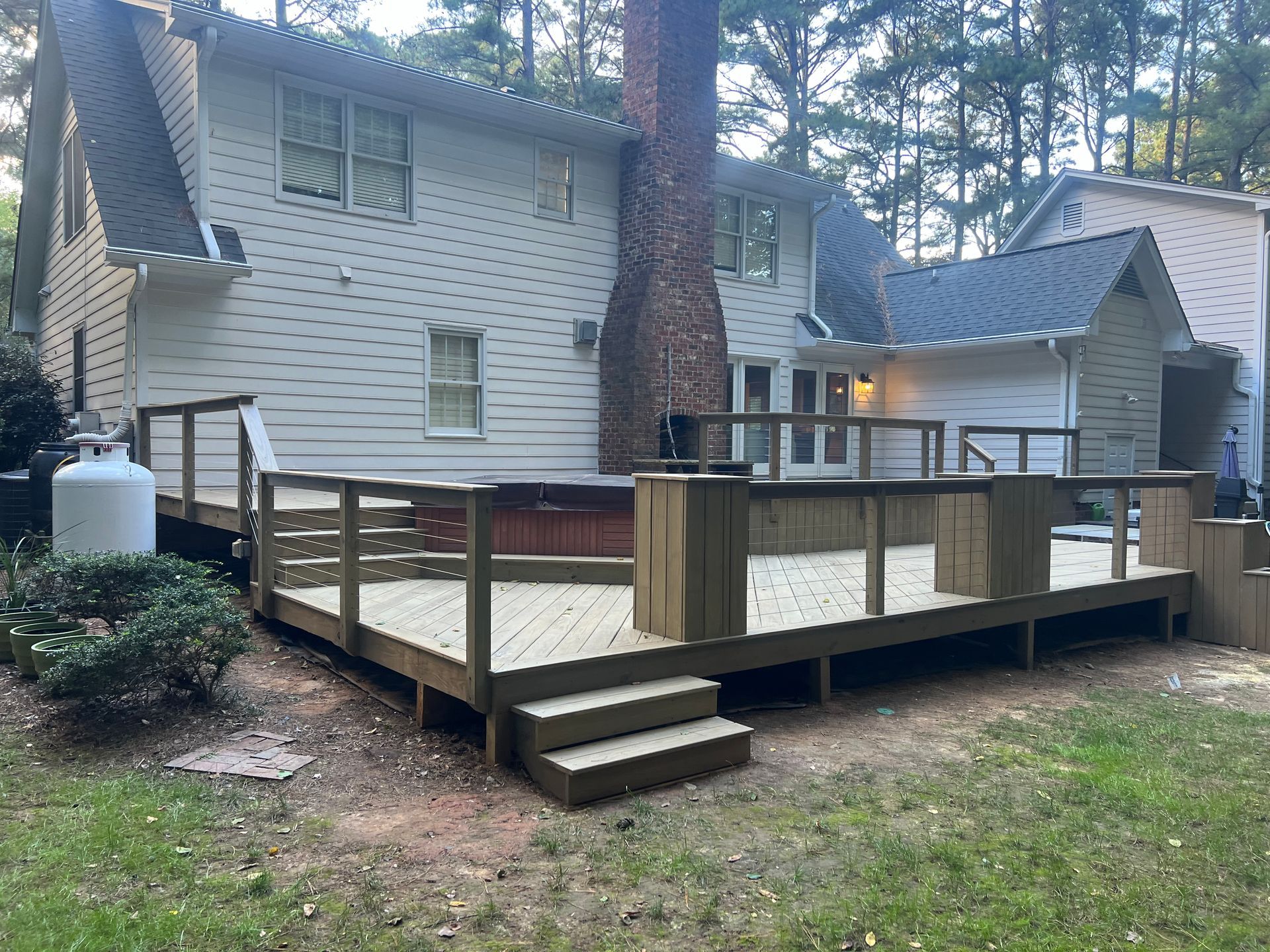 A multi-level wooden deck attached to a two-story house, with a hot tub and stairs.