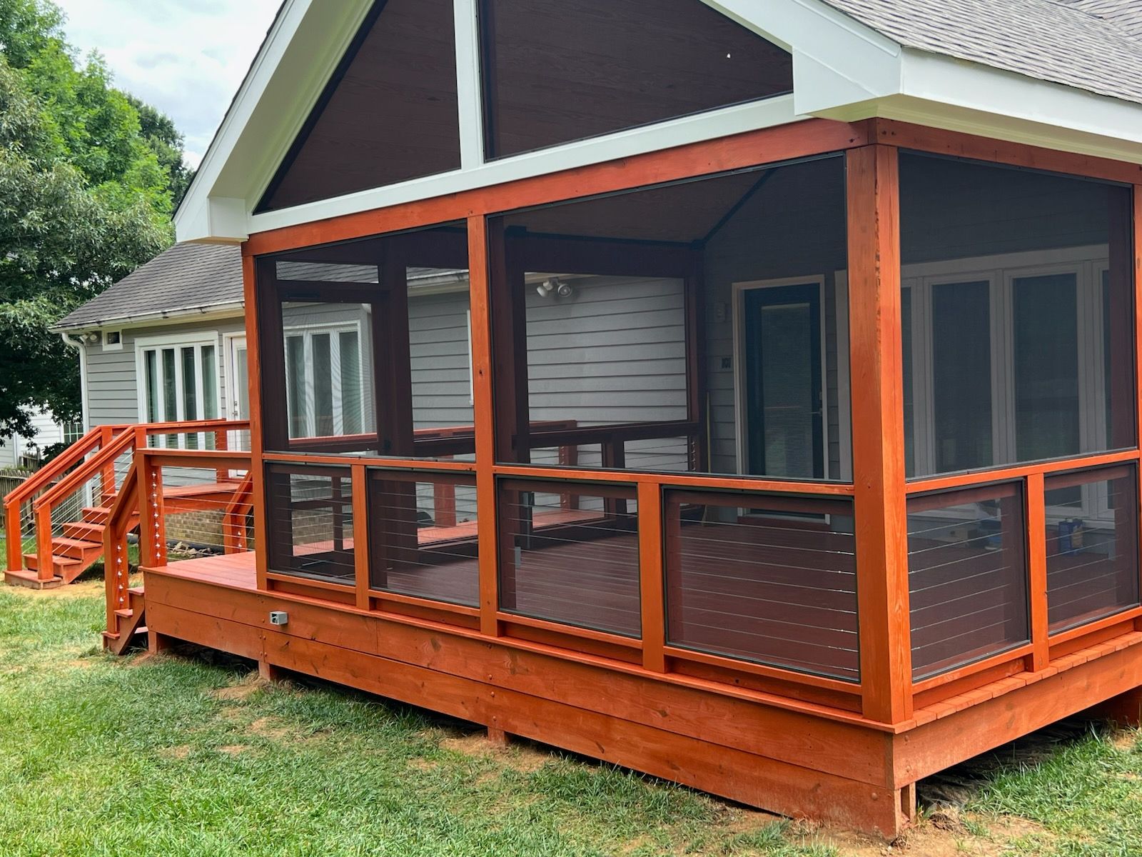 Screened-in porch and deck painted orange-red, attached to a gray house, with green grass in the foreground.