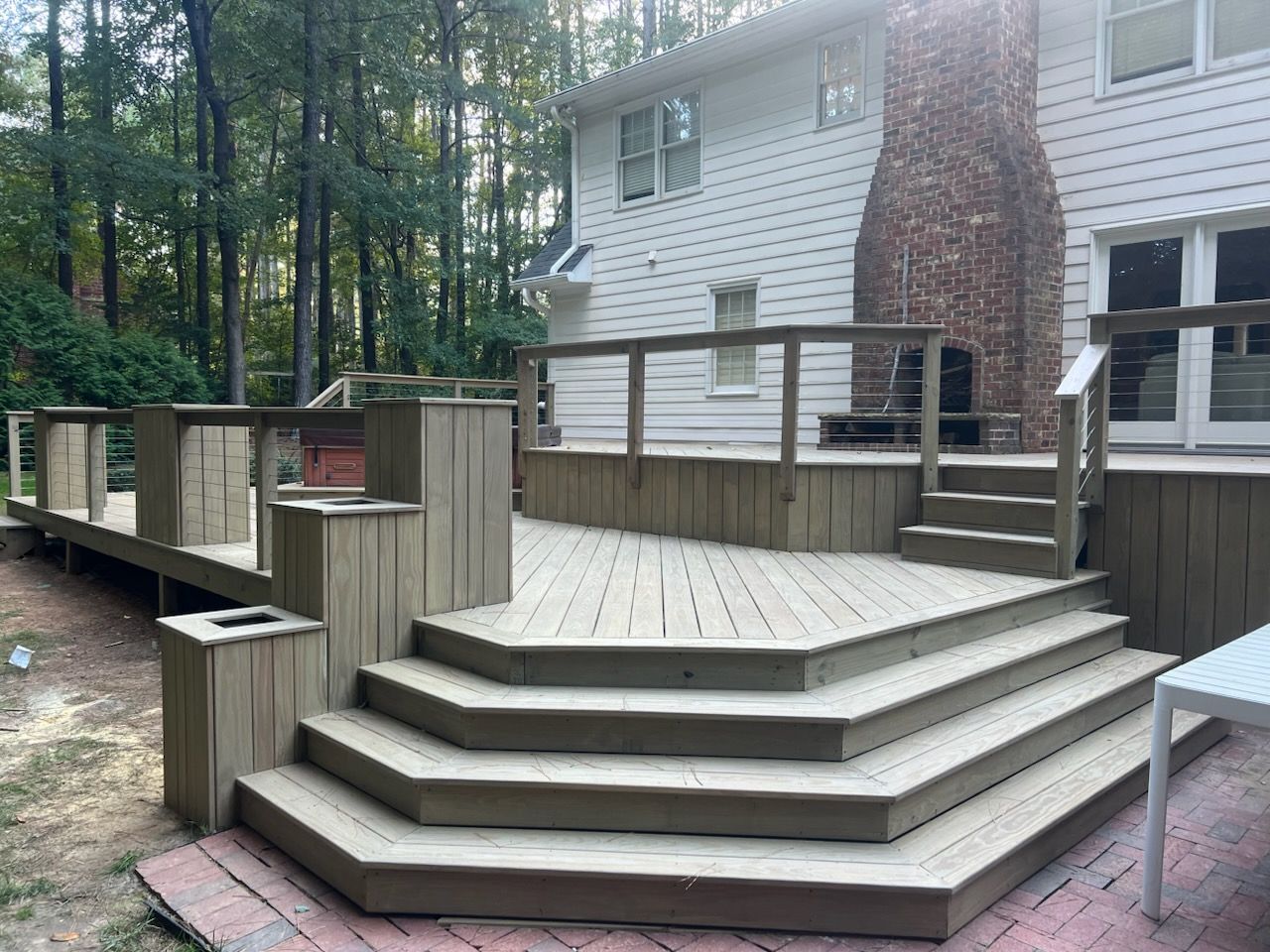 Wooden outdoor deck with steps and railing, attached to a light-colored house.