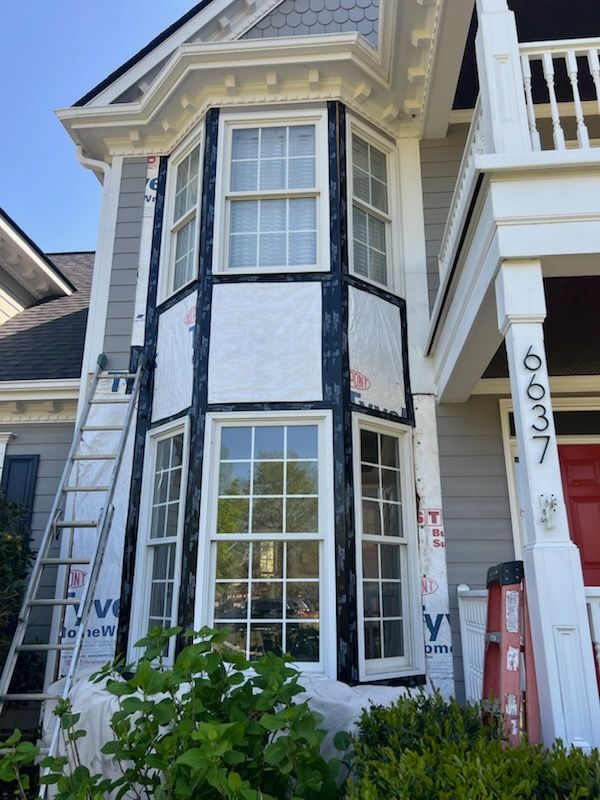 House exterior with bay window under construction; gray siding, white trim, ladder.