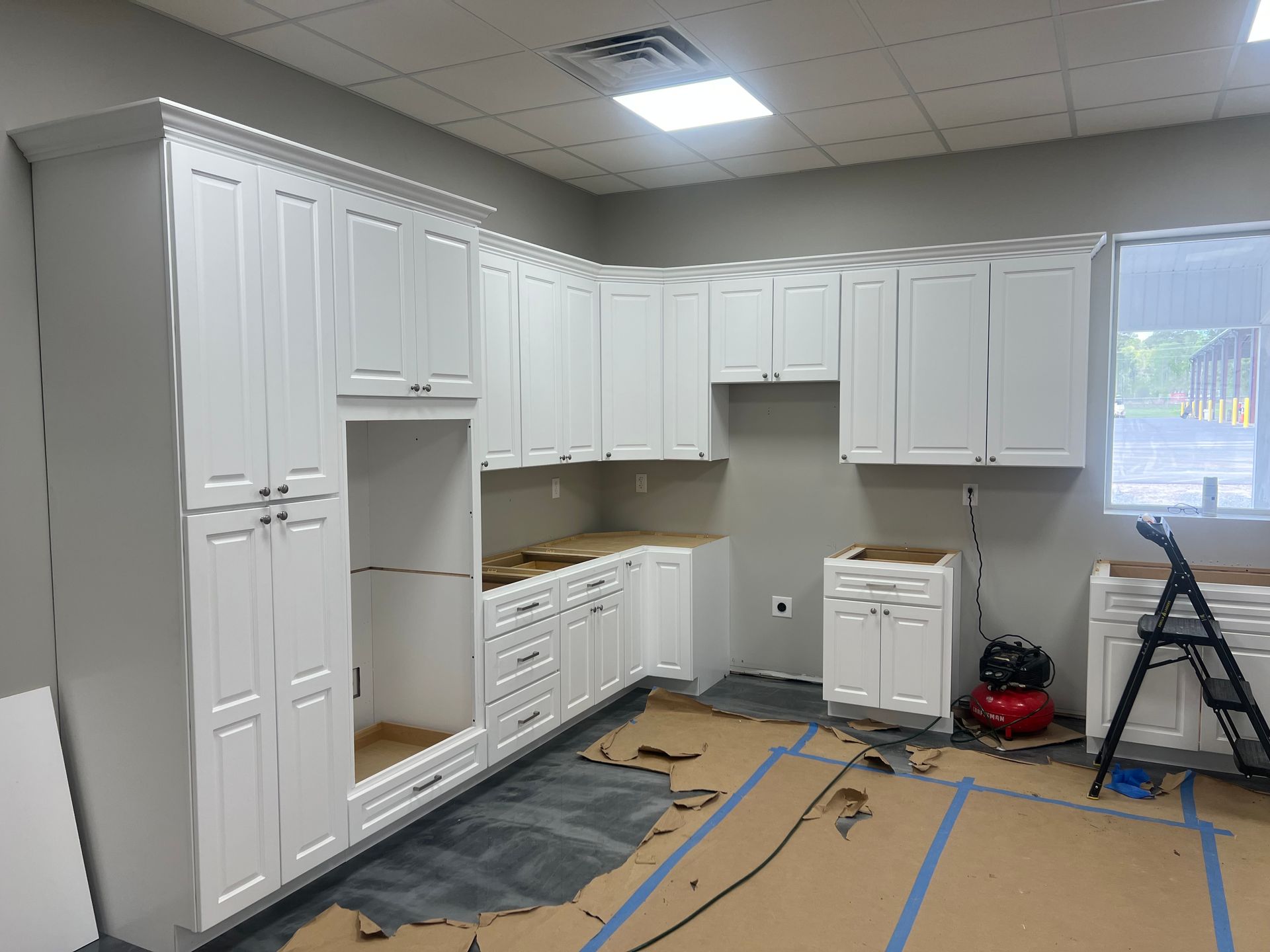 White kitchen cabinets installed in a room with cardboard on the floor, ready for countertops and appliances.