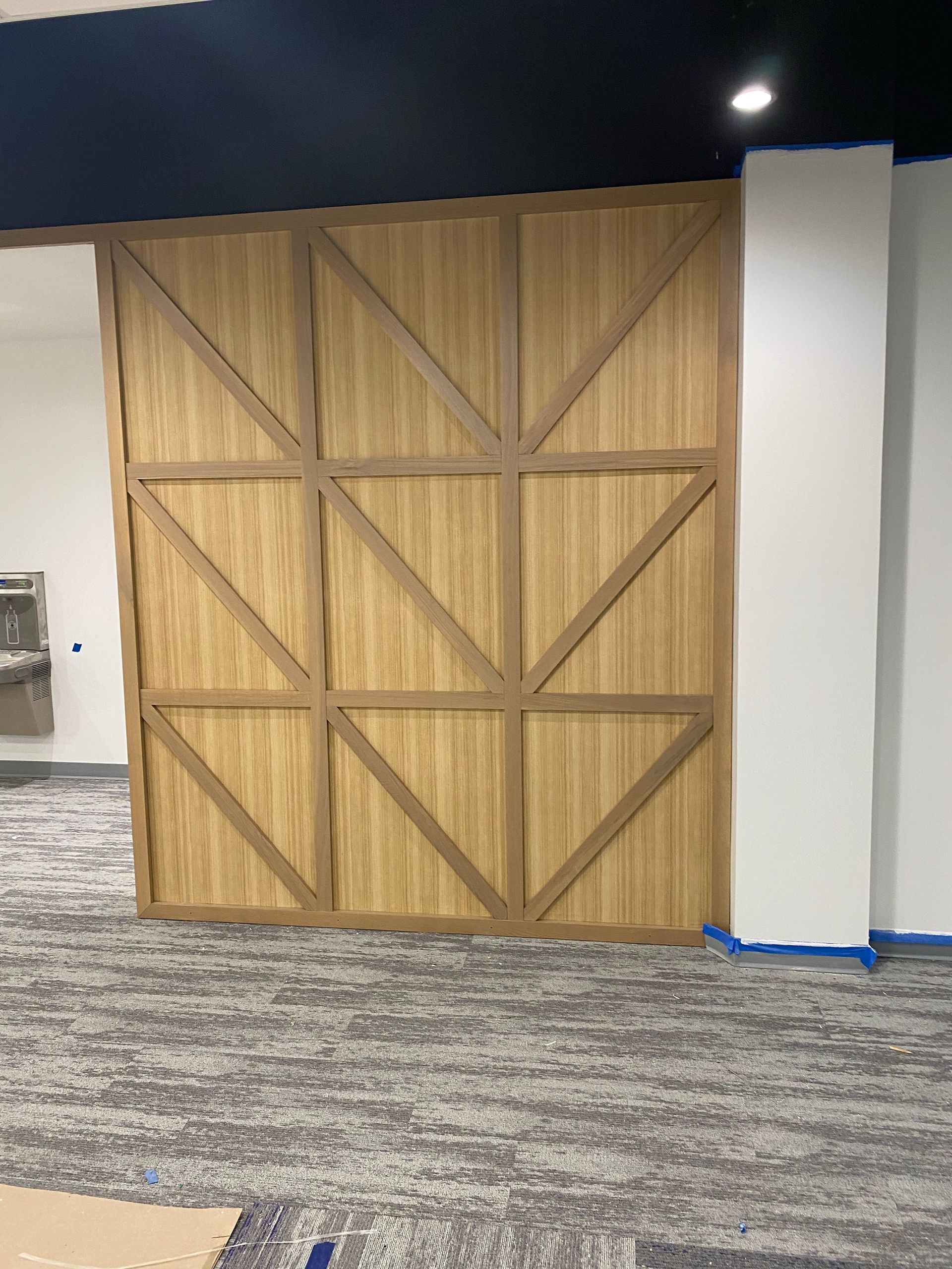 Wooden panel wall with geometric design, beige and brown, in a room with carpet and white columns.