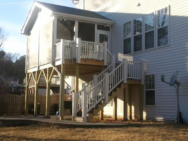 Two-story wooden deck with stairs and screened porch attached to a white house with multiple windows.